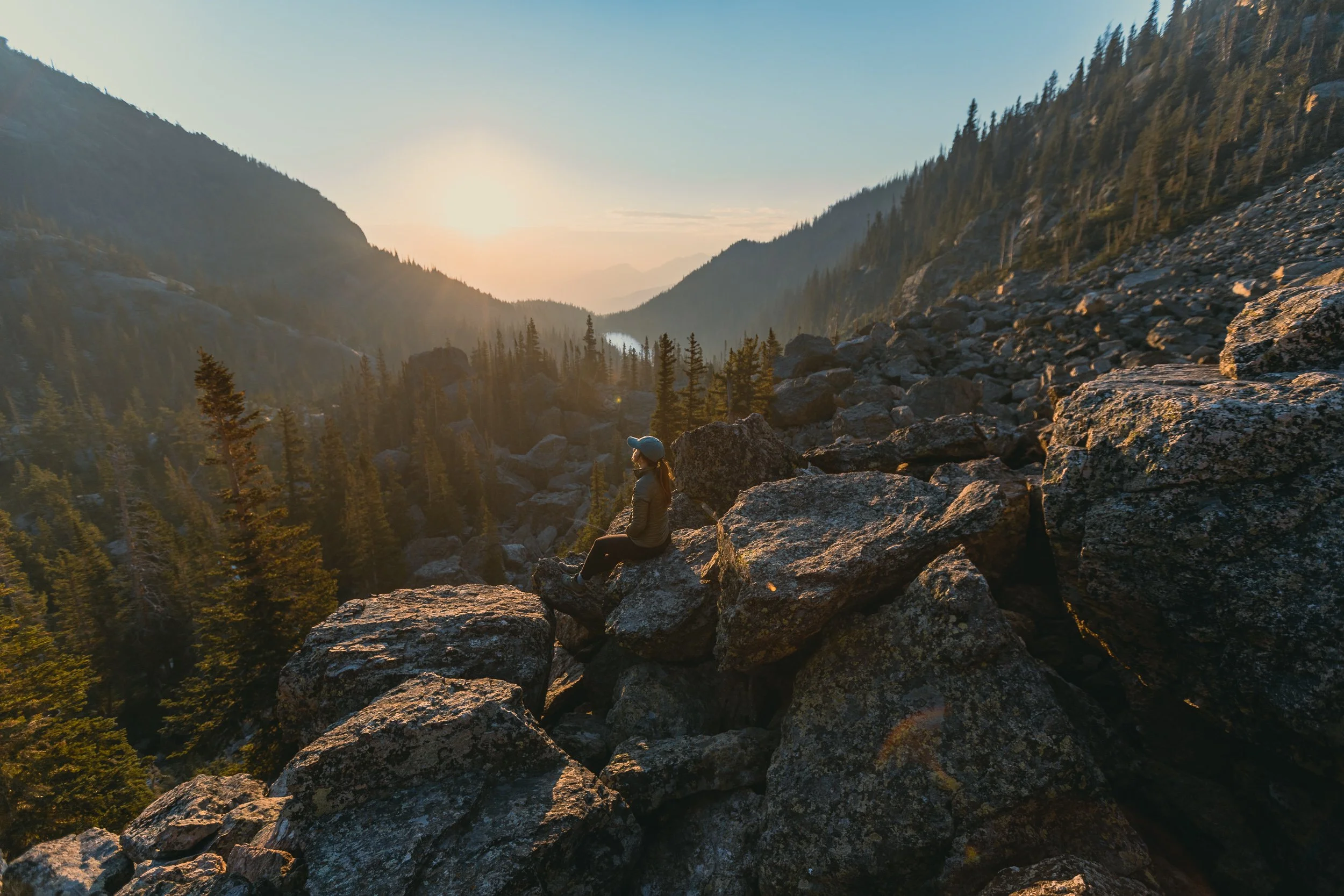  Hiker standing on rocky ridge at sunrise overlooking Dream Lake at Rocky Mountain National Park, adventure photography by James Brasier