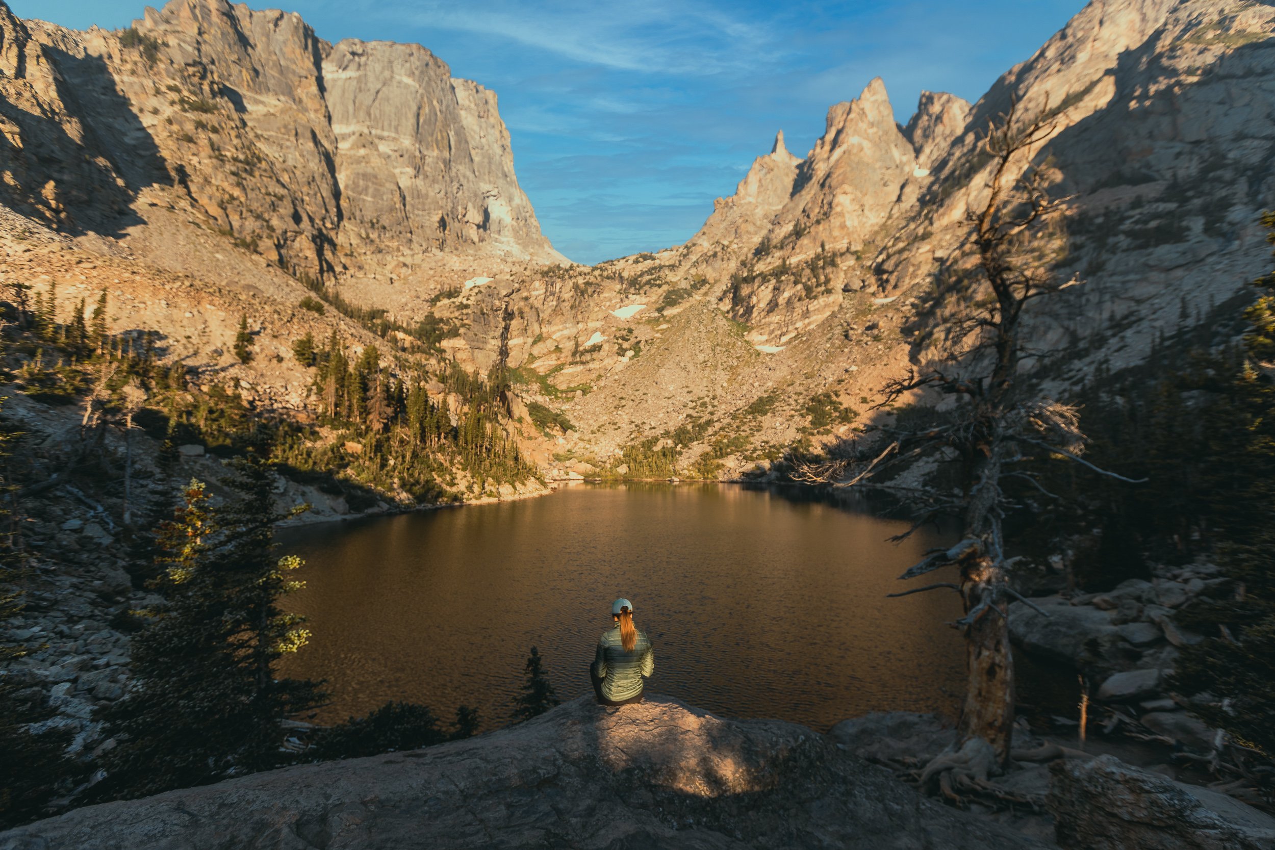 Person sitting at the edge of Emerald Lake surrounded by towering granite walls at Rocky Mountain National Park, Colorado landscape photography by James Brasier