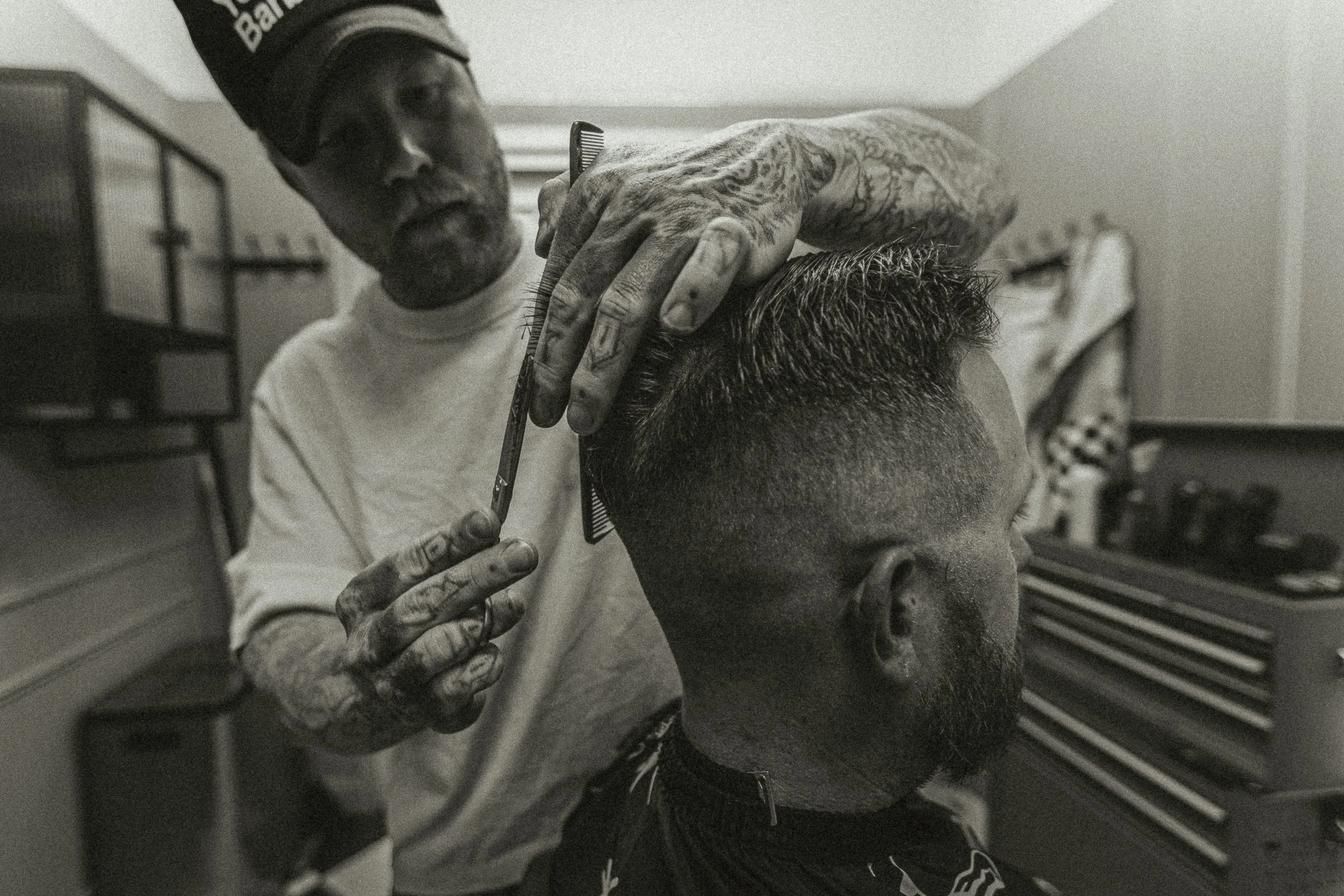 Tattooed barber hands cutting hair with scissors and comb at Artisan Grooming Parlor in black and white, commercial photography by James Brasier