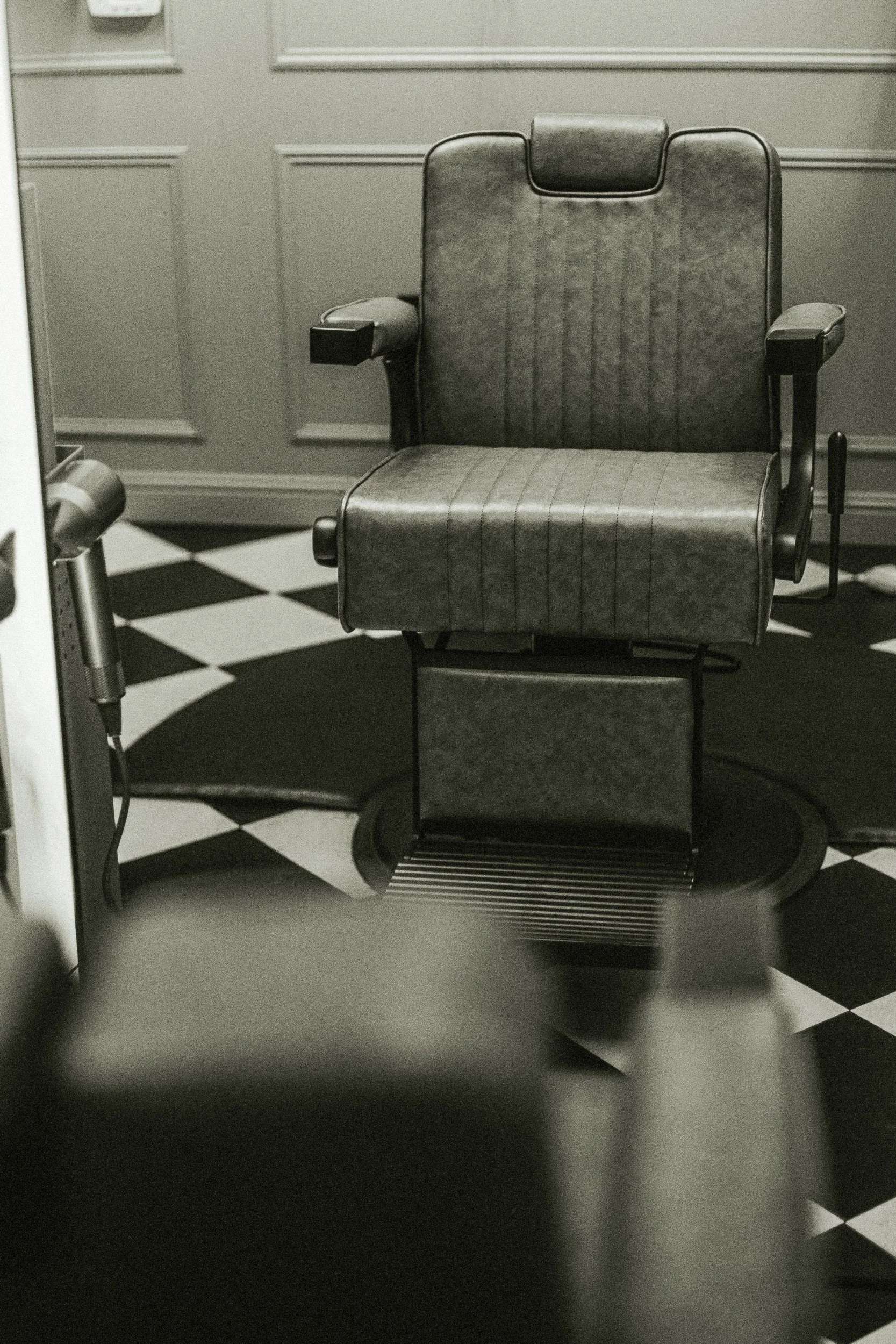 Empty leather barber chair on a checkerboard floor at Artisan Grooming Parlor in black and white, editorial interior photography by James Brasier