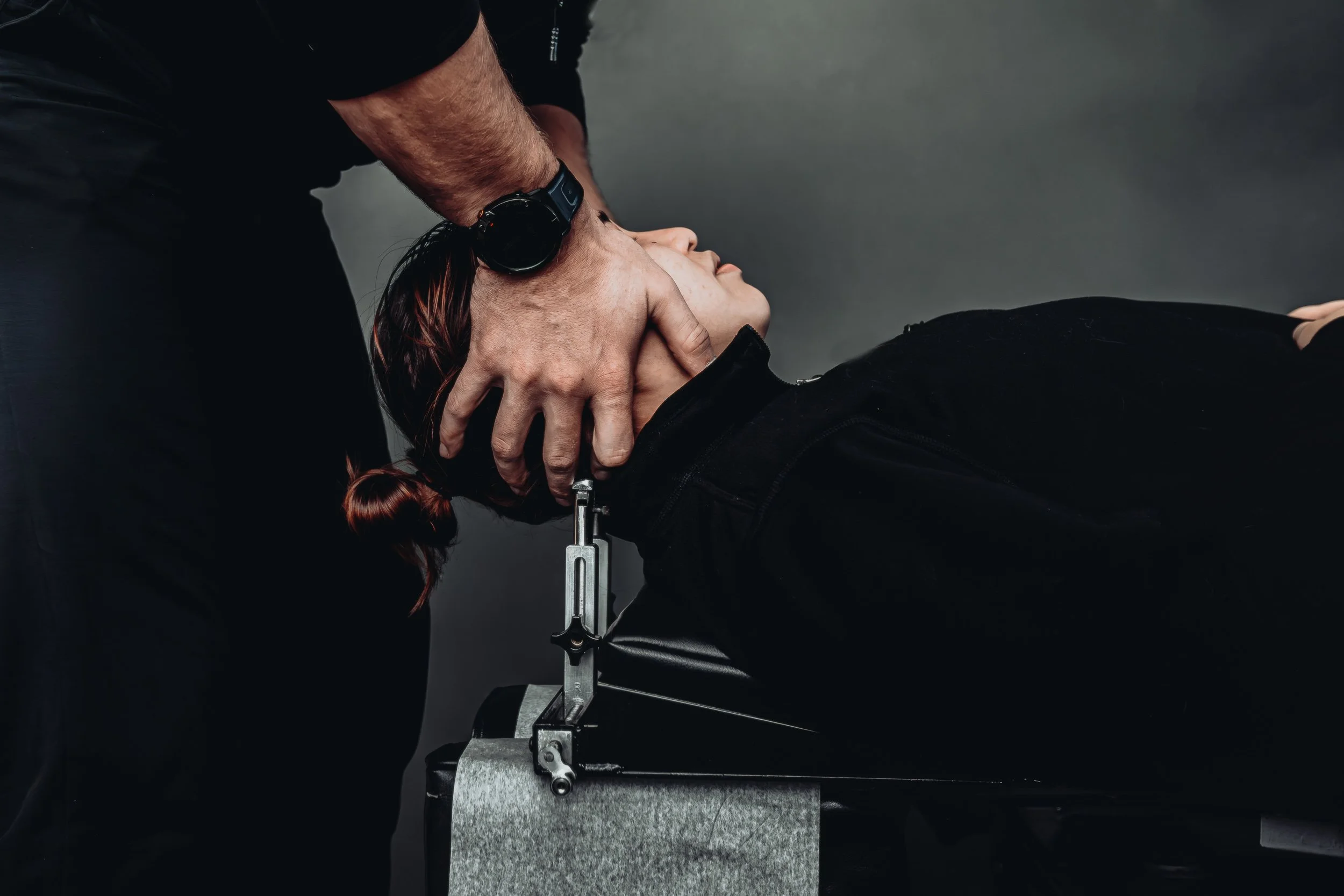 Chiropractor performing cervical adjustment in dark moody lighting at Square One Health, commercial photography by James Brasier