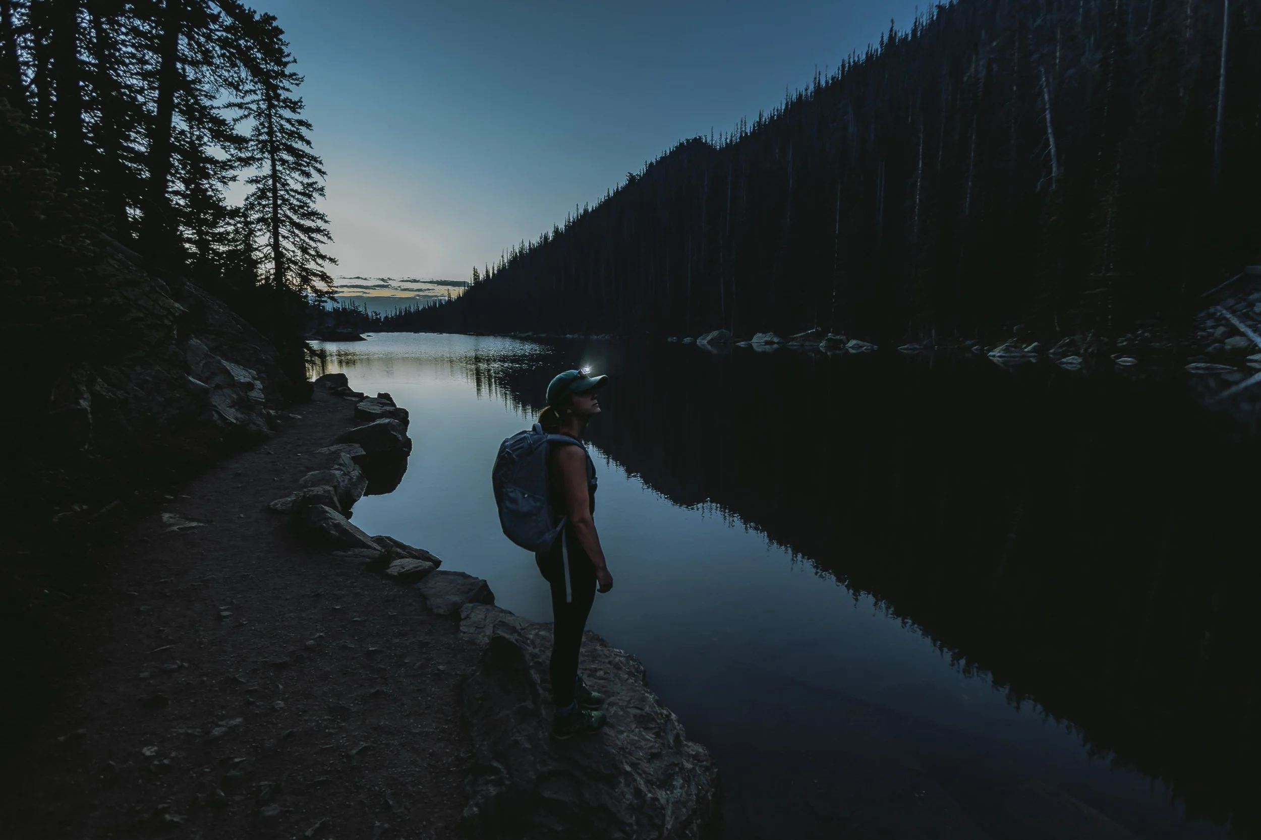 Hiker with headlamp standing at the edge of Dream Lake at blue hour in Rocky Mountain National Park, low light landscape photography by James Brasier