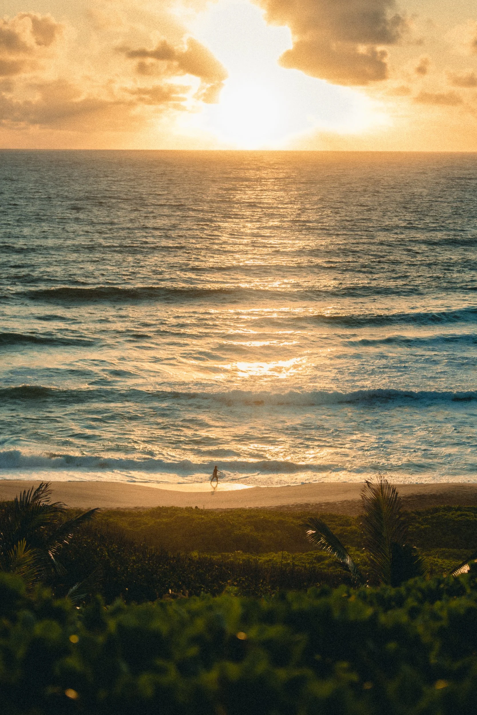 Person walking on the beach at sunrise with golden light reflecting off waves on the North Shore of Kauai Hawaii, sunrise photography by James Brasier