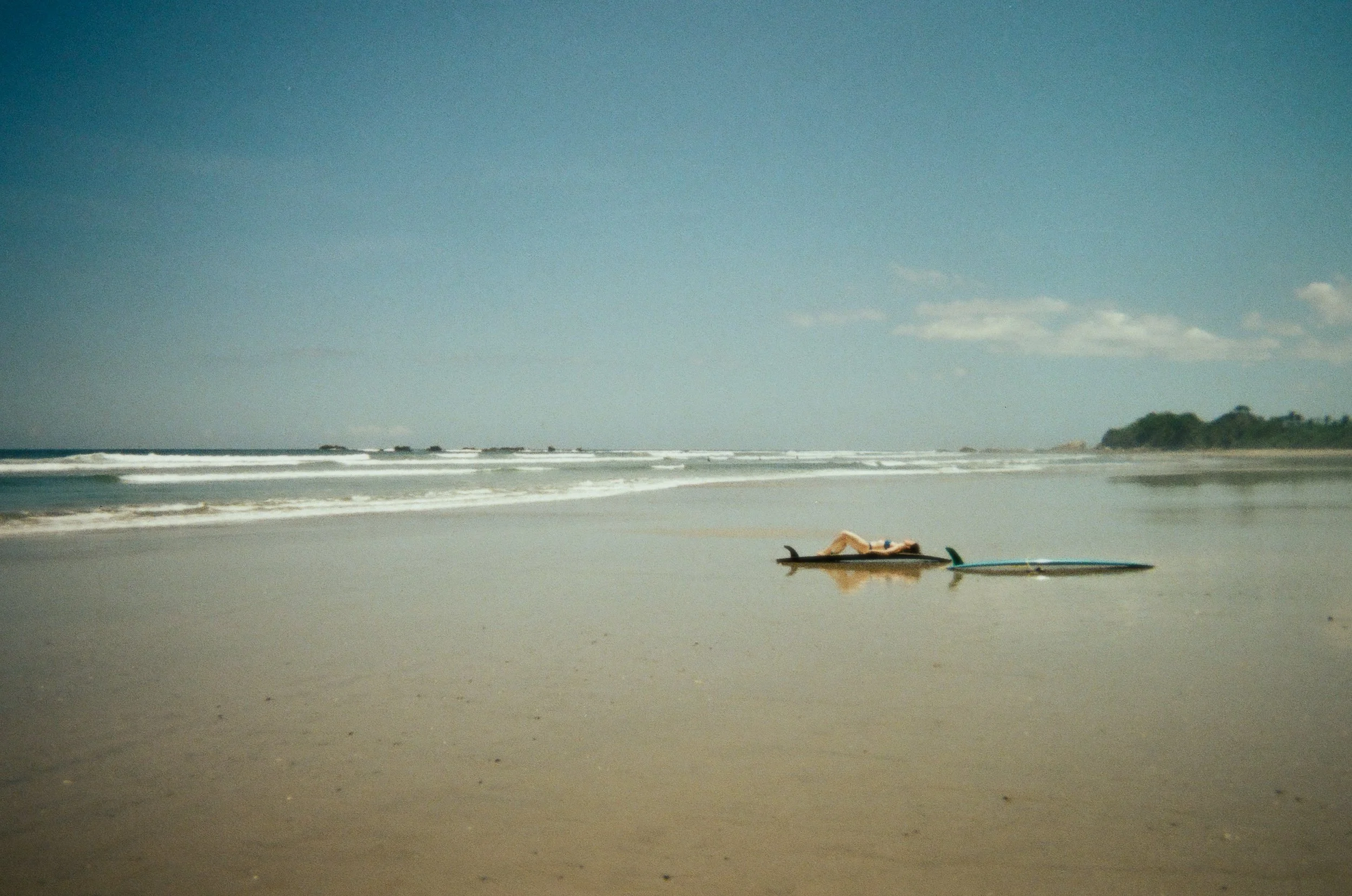 Person lying on a surfboard on the beach at Playa Guiones Costa Rica with warm film grain tones, surf lifestyle photography by James Brasier