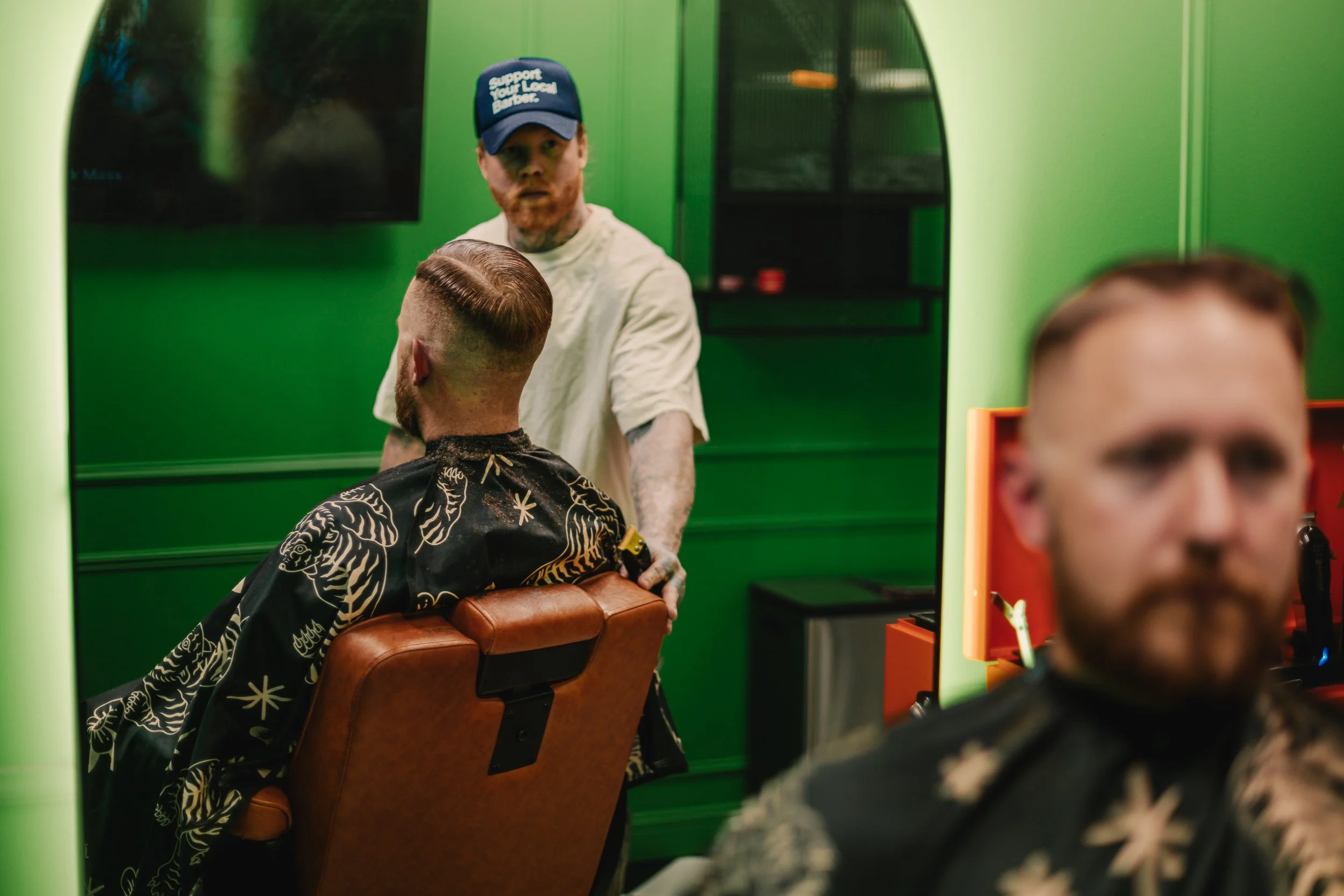 Barber working behind client in mirror reflection against green walls at Artisan Grooming Parlor, commercial photography by James Brasier