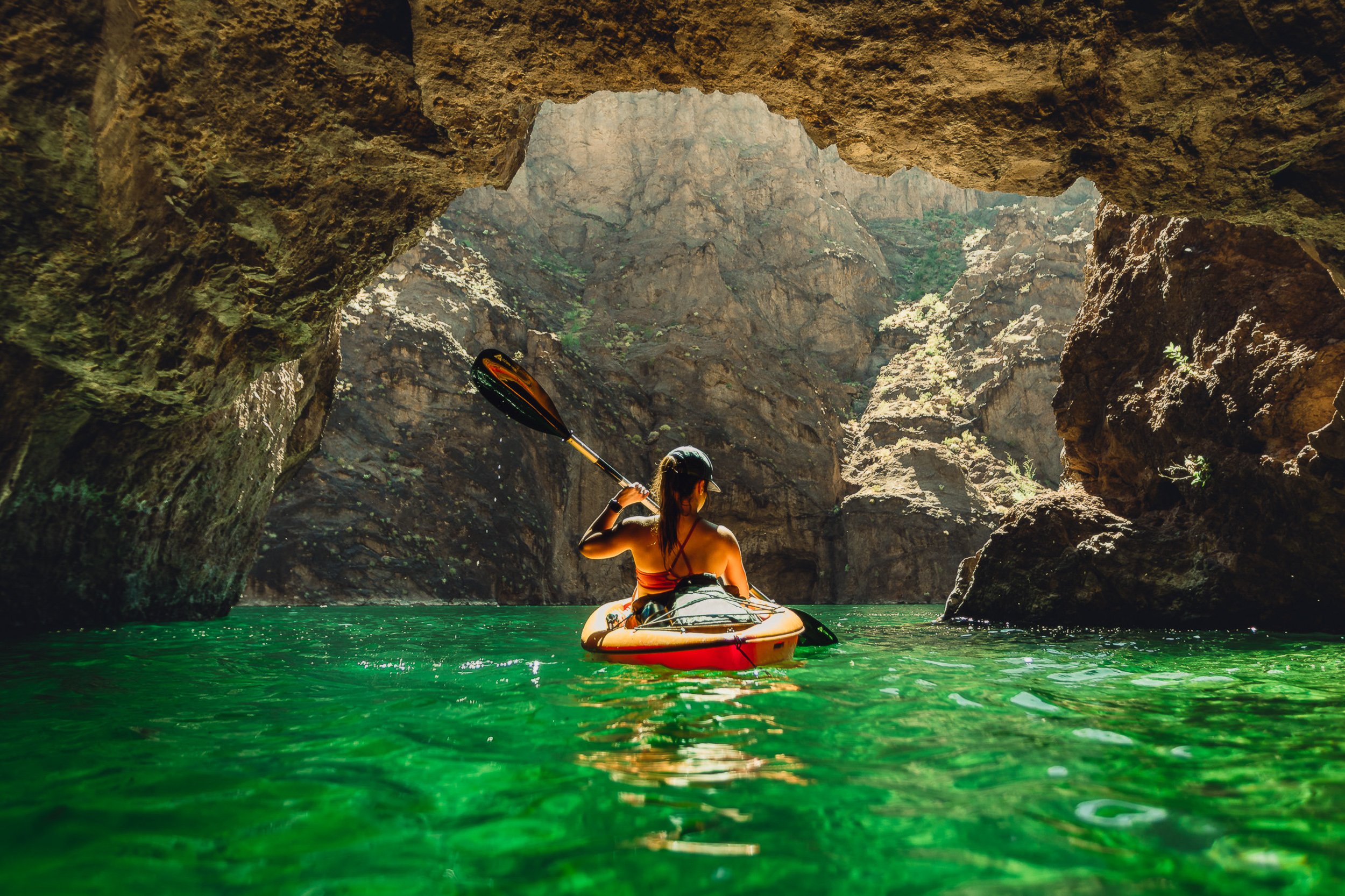 Kayaker in turquoise water beneath a rock arch at Emerald Cove on the Colorado River, Mojave Desert adventure photography by James Brasier