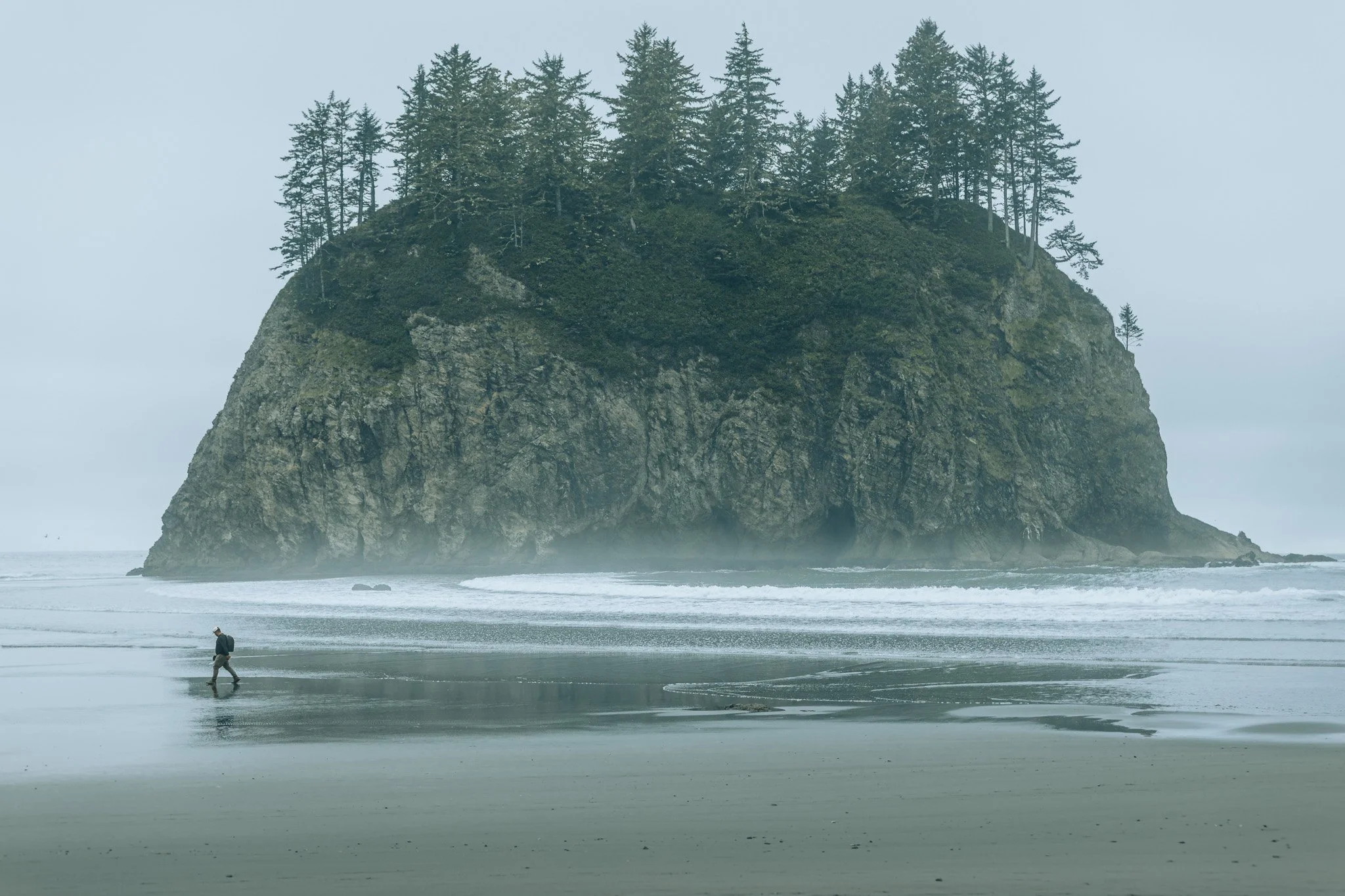 Hiker walking on foggy beach toward sea stack on the Olympic Peninsula, Washington, adventure travel photography