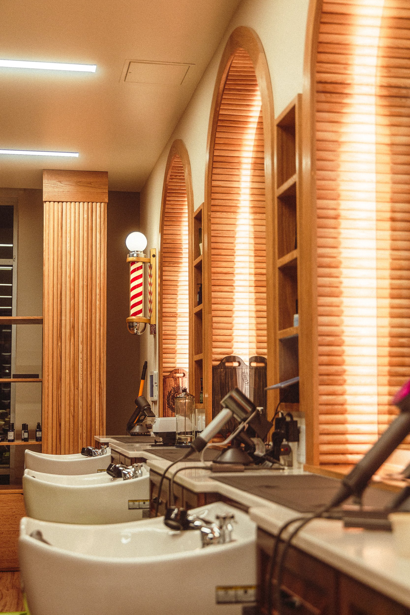 Row of barber stations and wash basins with arched mirrors and barber pole at The Rosemont Barbers, commercial interior photography by James Brasier