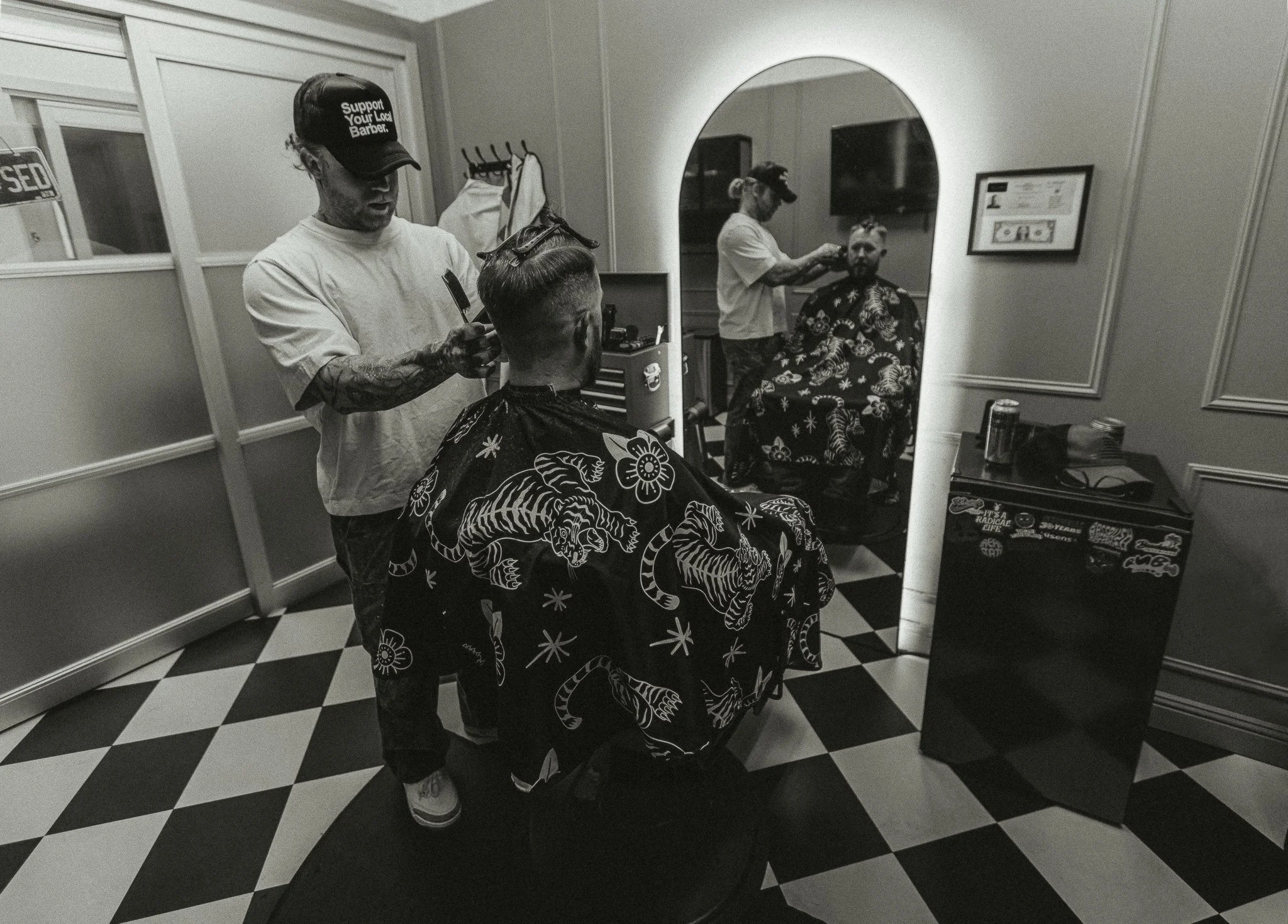 Black and white interior of Artisan Grooming Parlor with barber and client, checkerboard floor, commercial photography