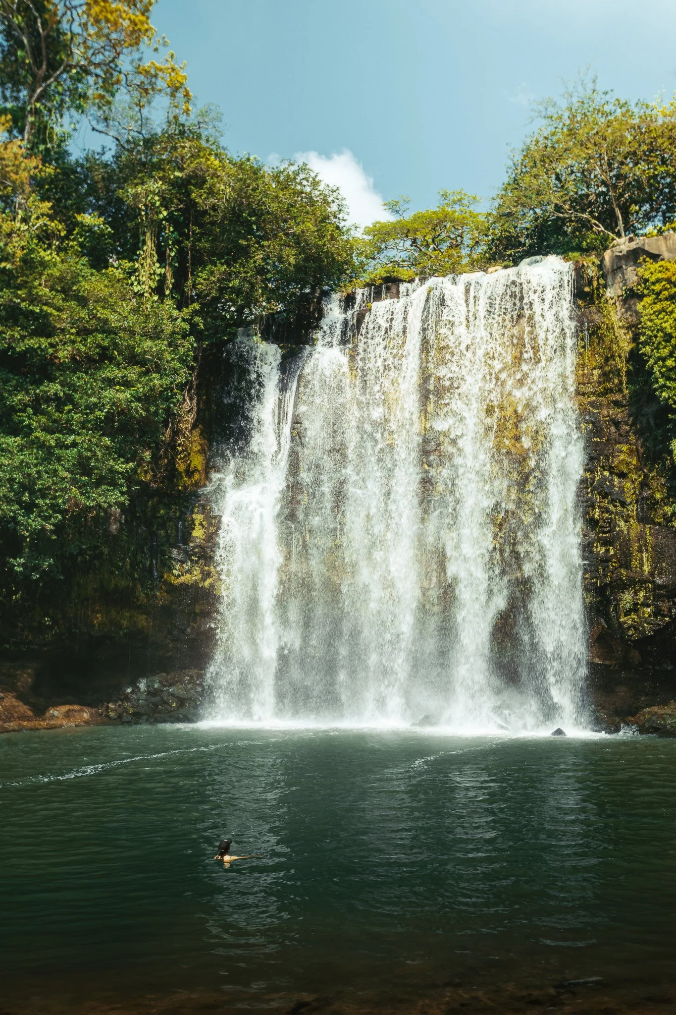 Swimmer beneath Llanos de Cortez waterfall in Costa Rica, adventure travel landscape photography