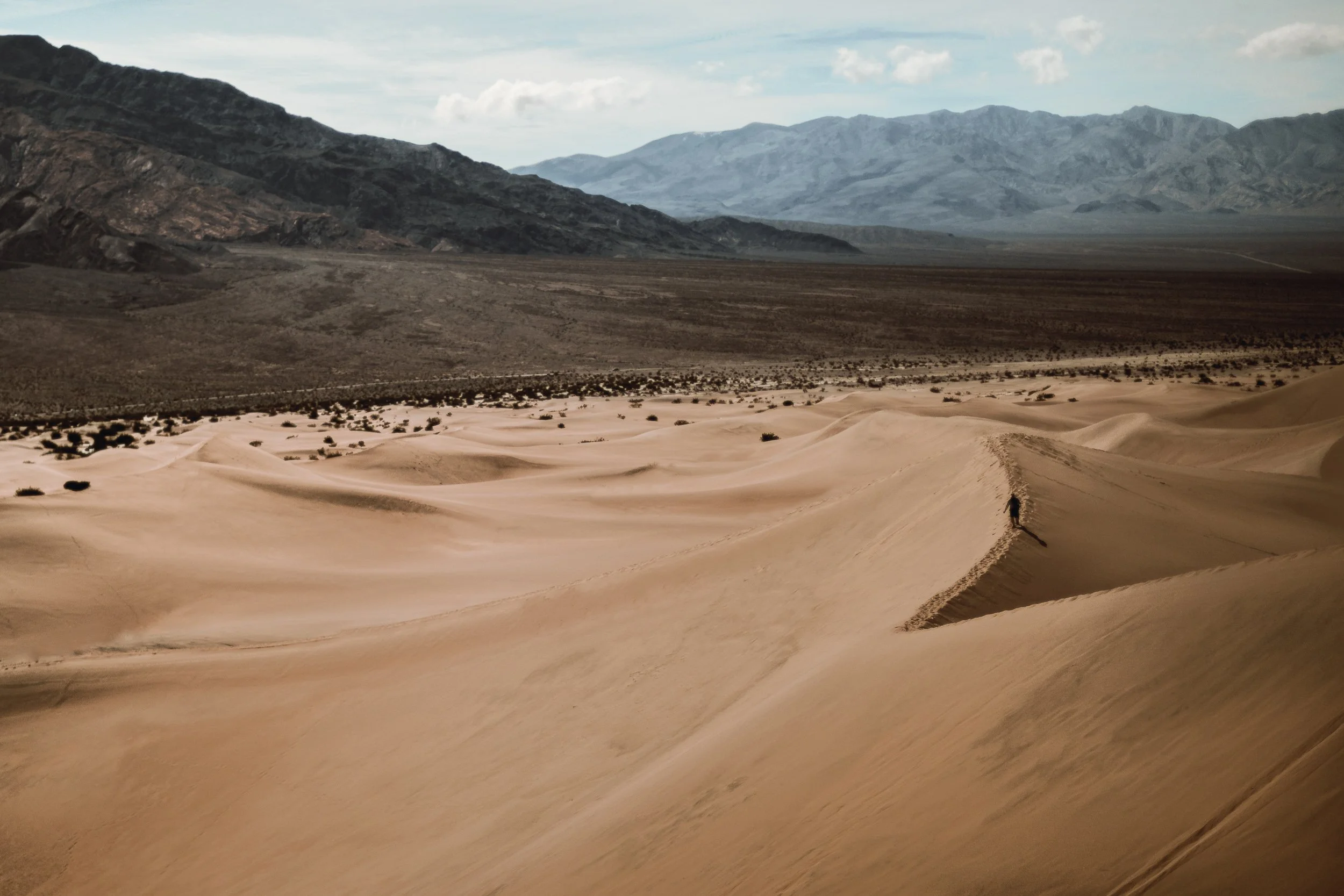 Vast sand dunes stretching toward distant mountains at Death Valley in the Mojave Desert, outdoor landscape photography by James Brasier
