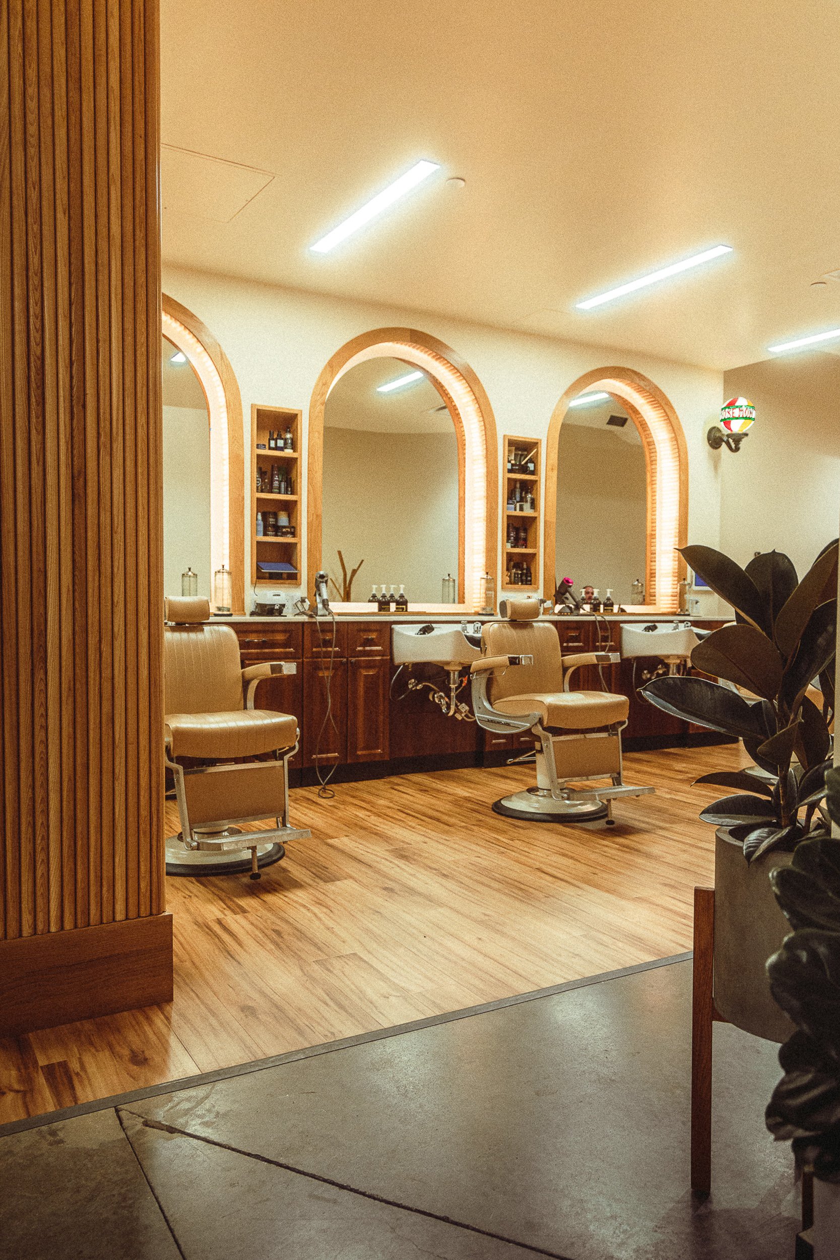 The Rosemont Barbers interior framed through a wooden doorway with barber chairs and arched mirrors in warm light, commercial interior photography by James Brasier