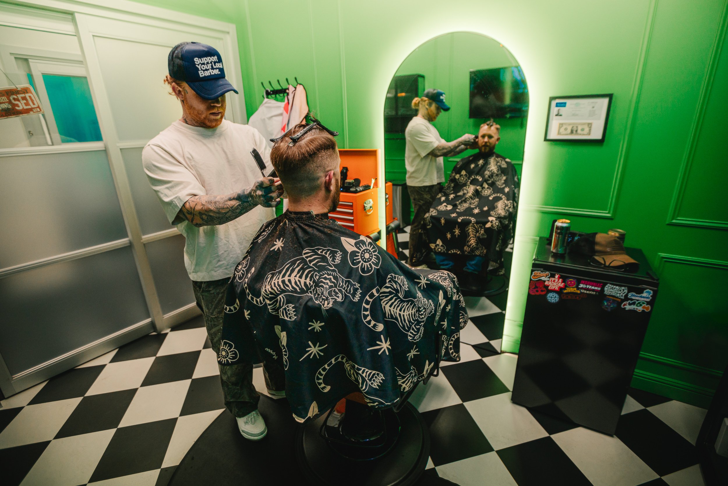 Wide interior of Artisan Grooming Parlor with checkerboard floor and green walls during a haircut with mirror reflection, commercial interior photography by James Brasier