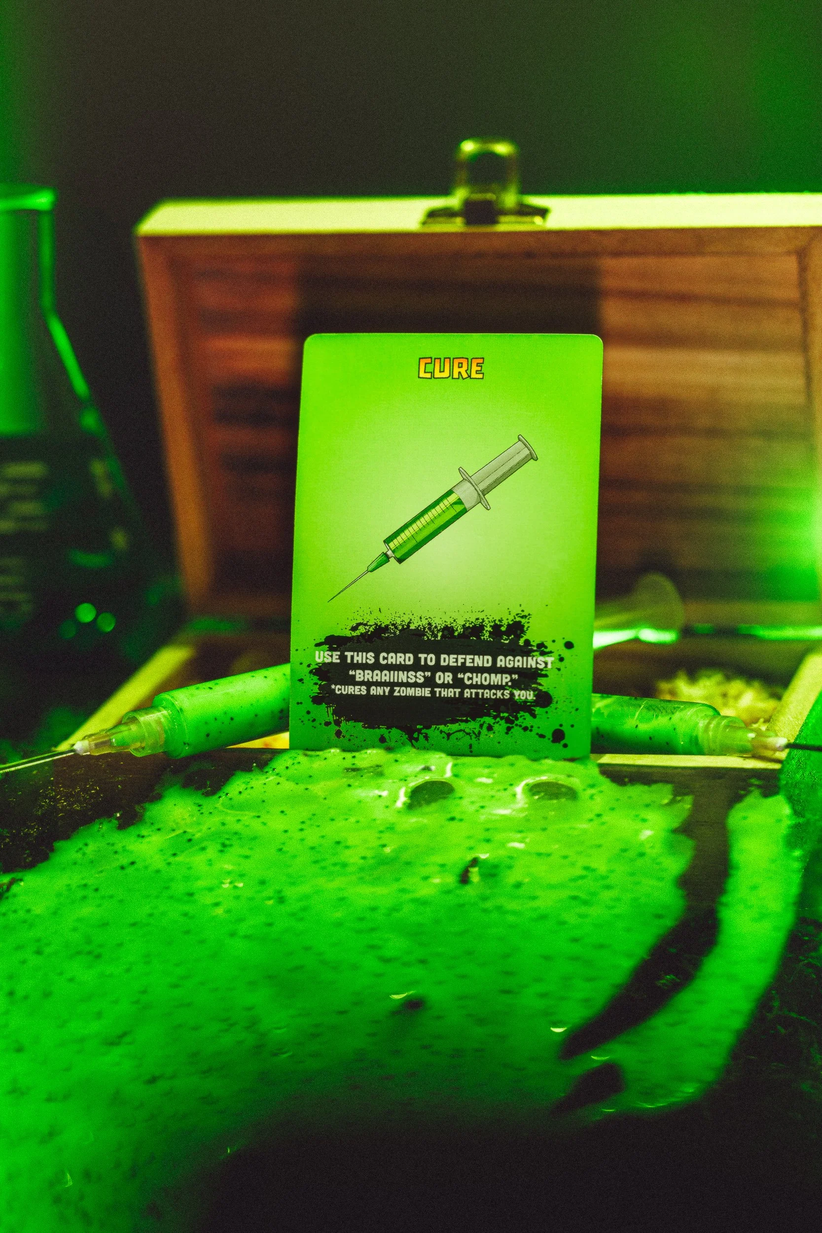 ZETA Survival Cure card styled in green laboratory scene with bubbling liquid and syringes, product photography by James Brasier