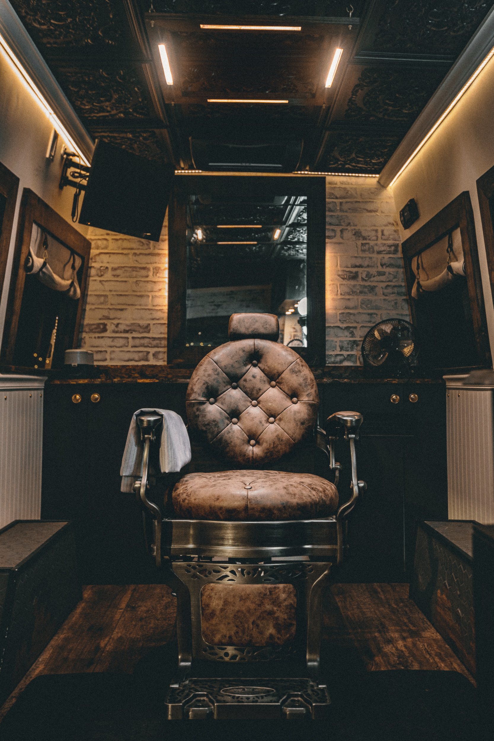 Vintage leather barber chair centered in the Nomad Mobile Barbershop van interior with tin ceiling and brick accent wall, commercial interior photography by James Brasier