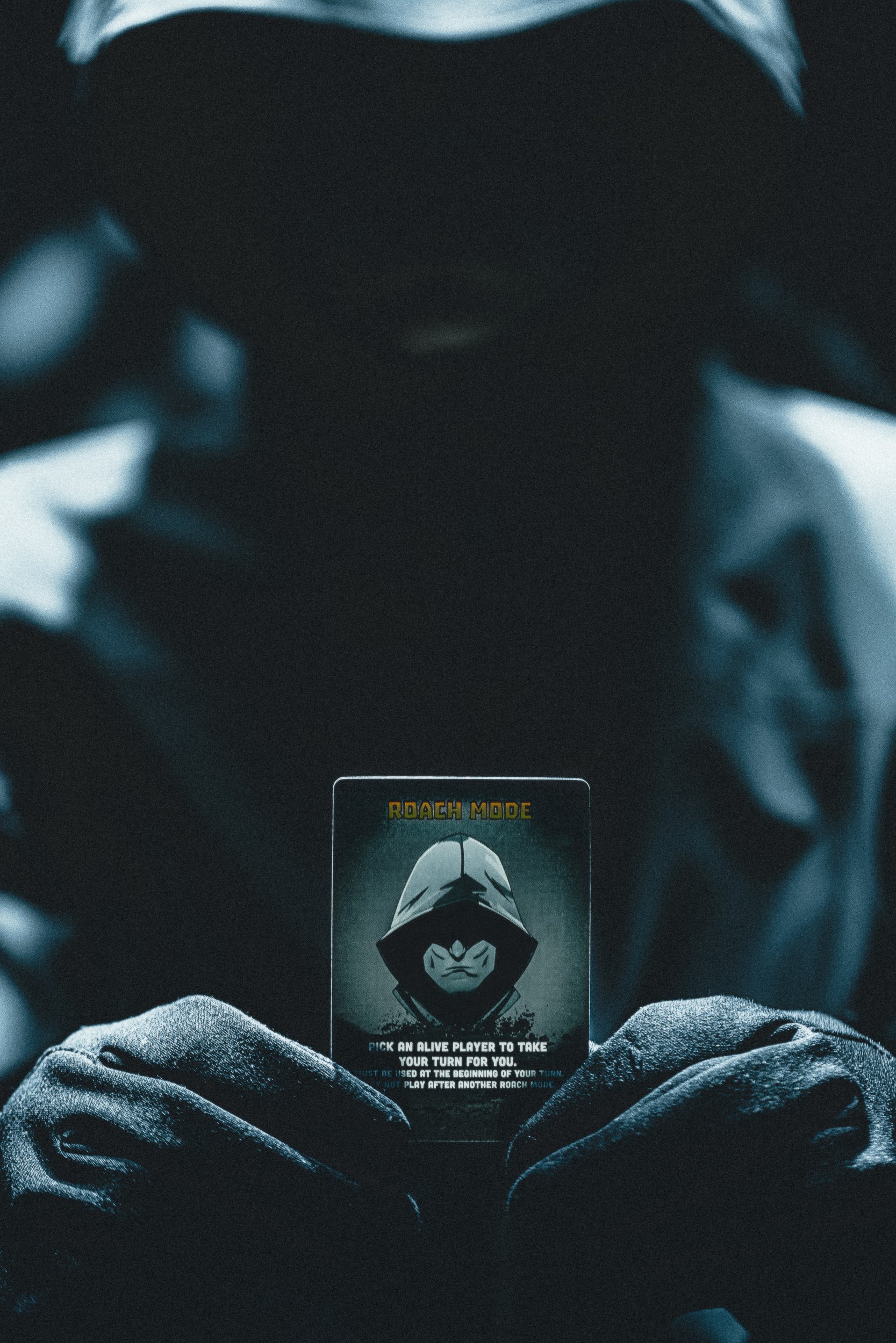 Hooded figure holding ZETA Survival Roach Mode card in dark cinematic blue tones, product campaign photography by James Brasier
