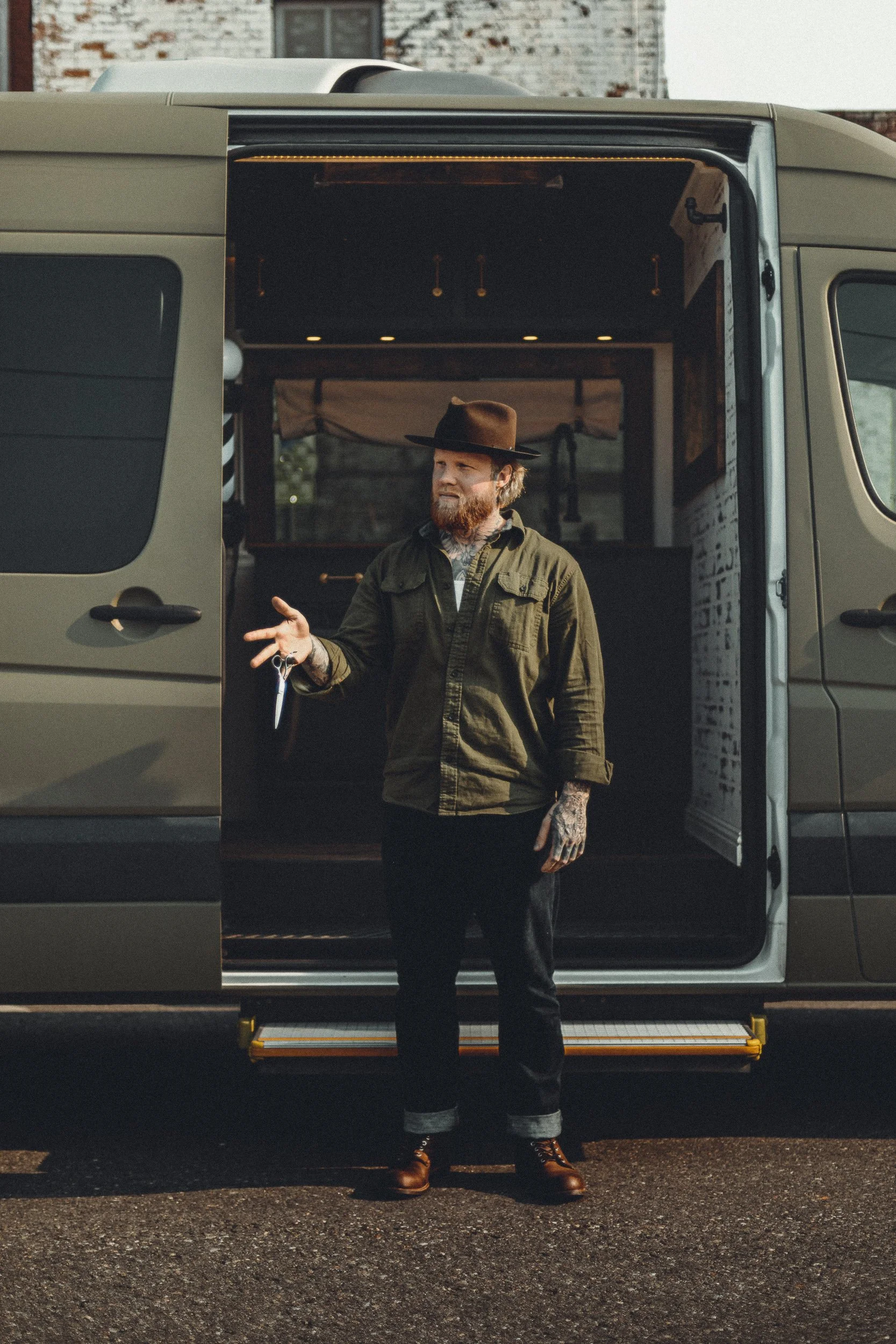 Nomad Mobile Barbershop barber flipping metal shears outside the van with the interior visible through the open door, brand portrait photography by James Brasier