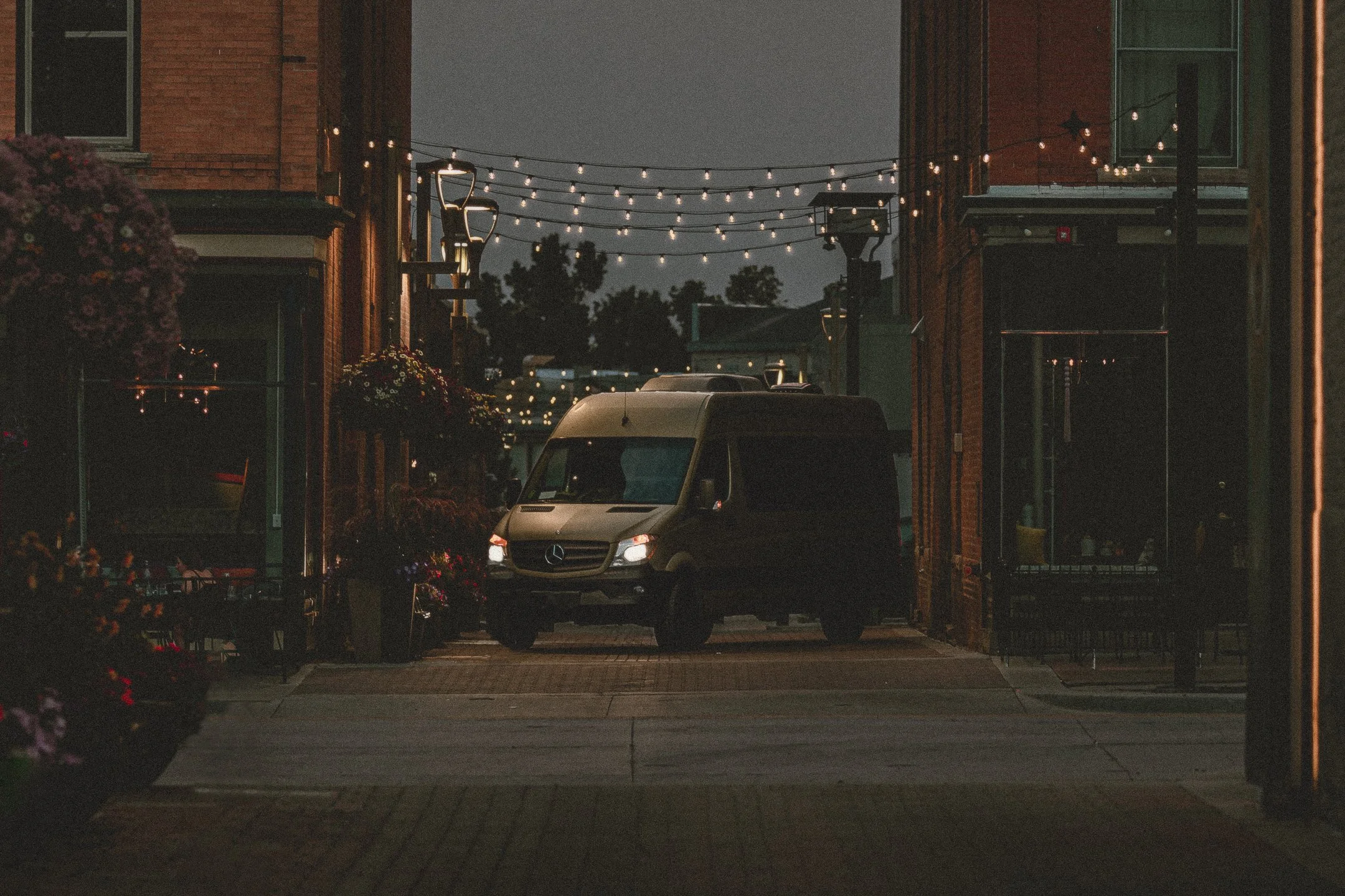 Nomad Mobile Barbershop van framed by string lights in downtown alley at dusk, brand photography by James Brasier