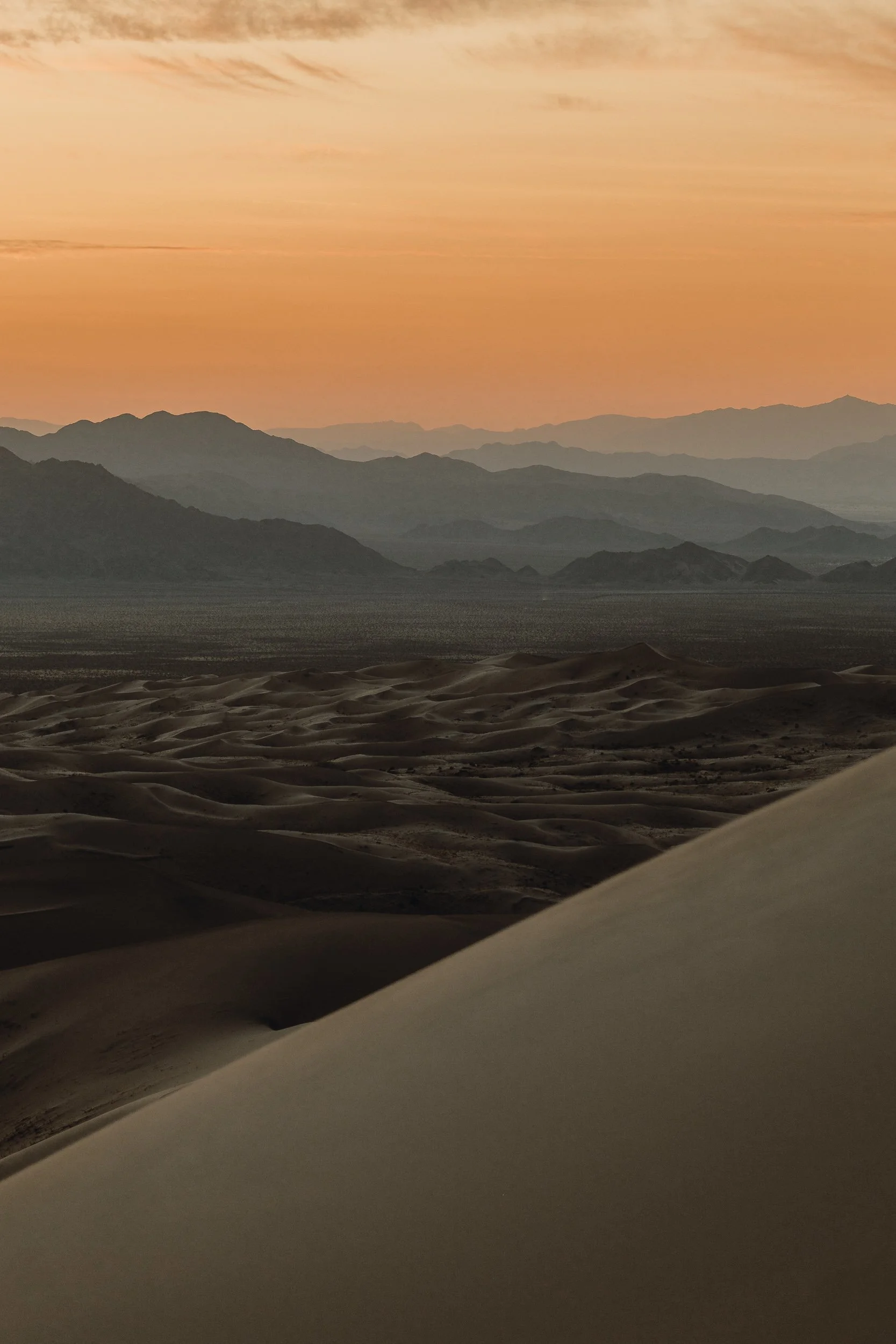 Sunset over layered desert mountains viewed from the ridge of Kelso Dunes in the Mojave Desert, landscape photography by James Brasier