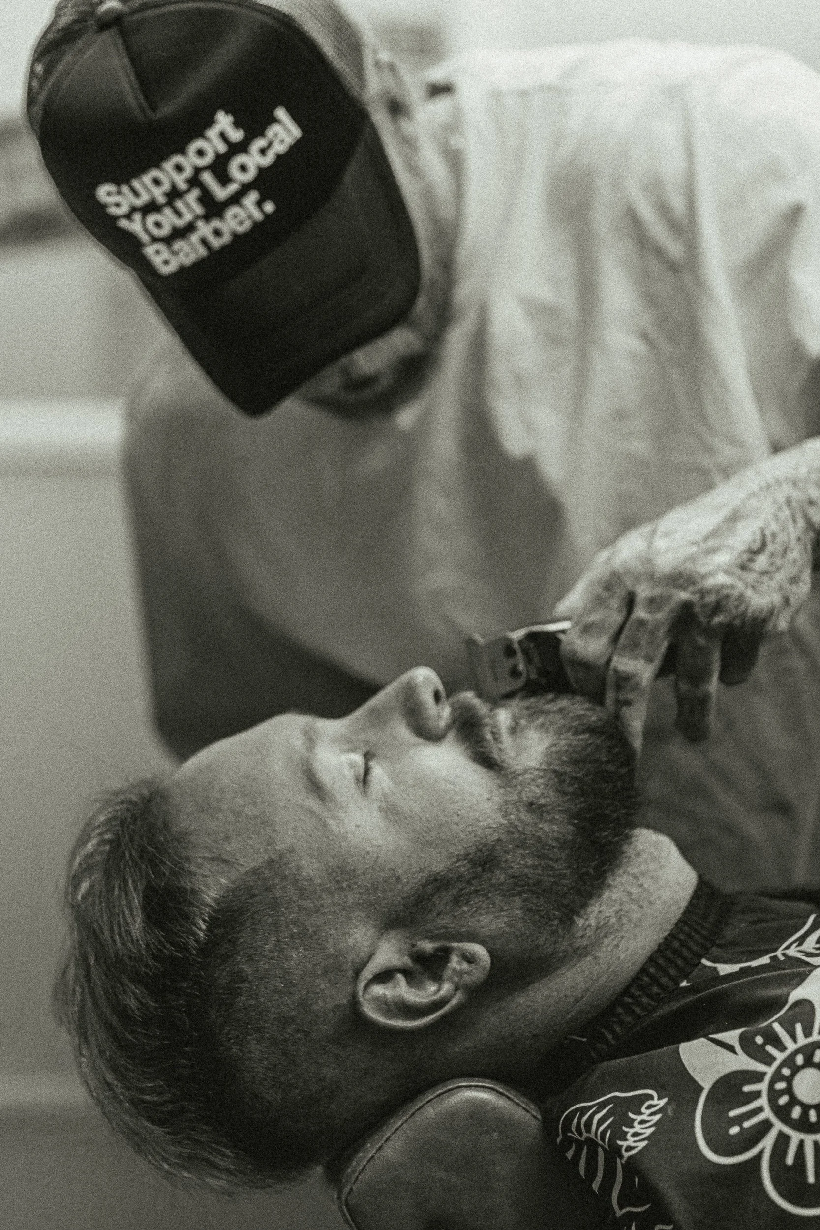 Close-up of barber trimming a beard with clippers at Artisan Grooming Parlor in black and white, commercial photography by James Brasier