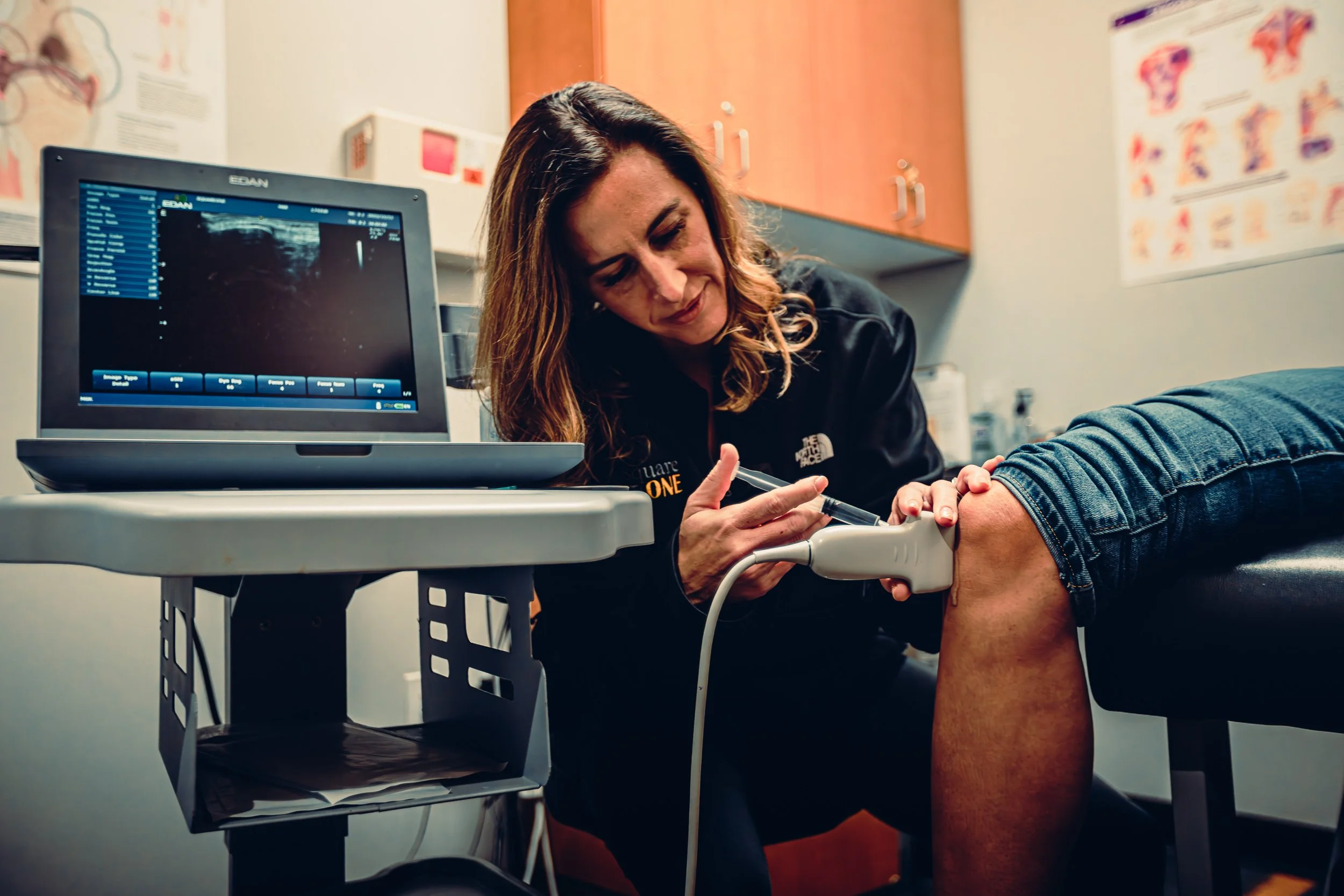 Practitioner performing ultrasound-guided knee injection with imaging screen at Square One Health, commercial photography by James Brasier