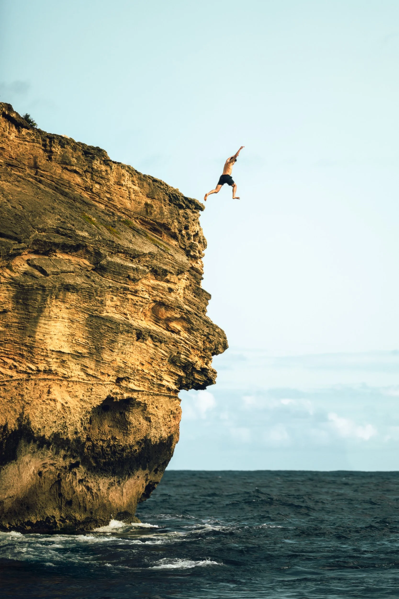 Person jumping off a golden sandstone cliff into the ocean at Shipwreck Beach, Kauai Hawaii adventure photography by James Brasier