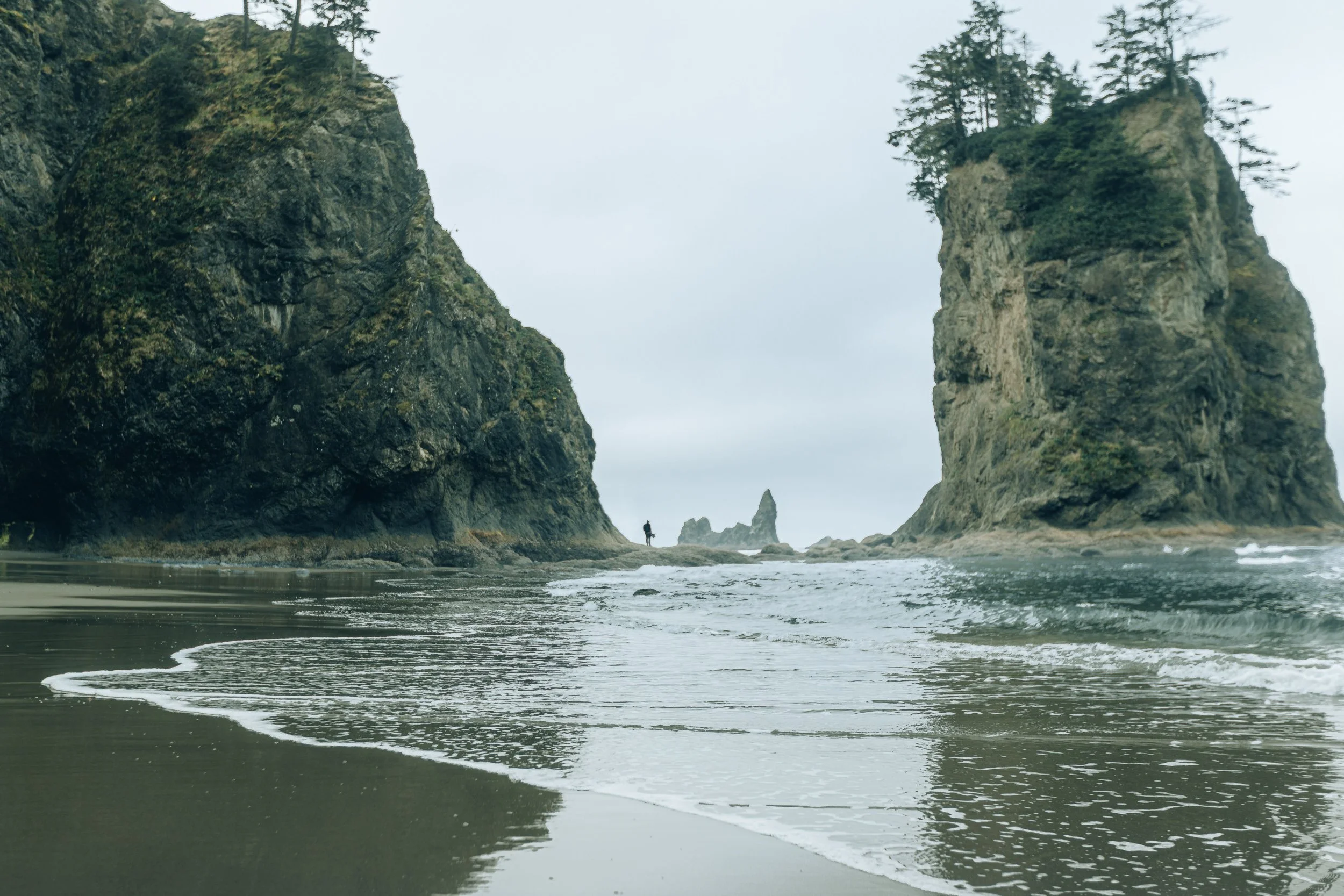 Tide water flowing between towering sea stacks with a figure silhouetted in the distance on the Olympic Peninsula, coastal landscape photography by James Brasier