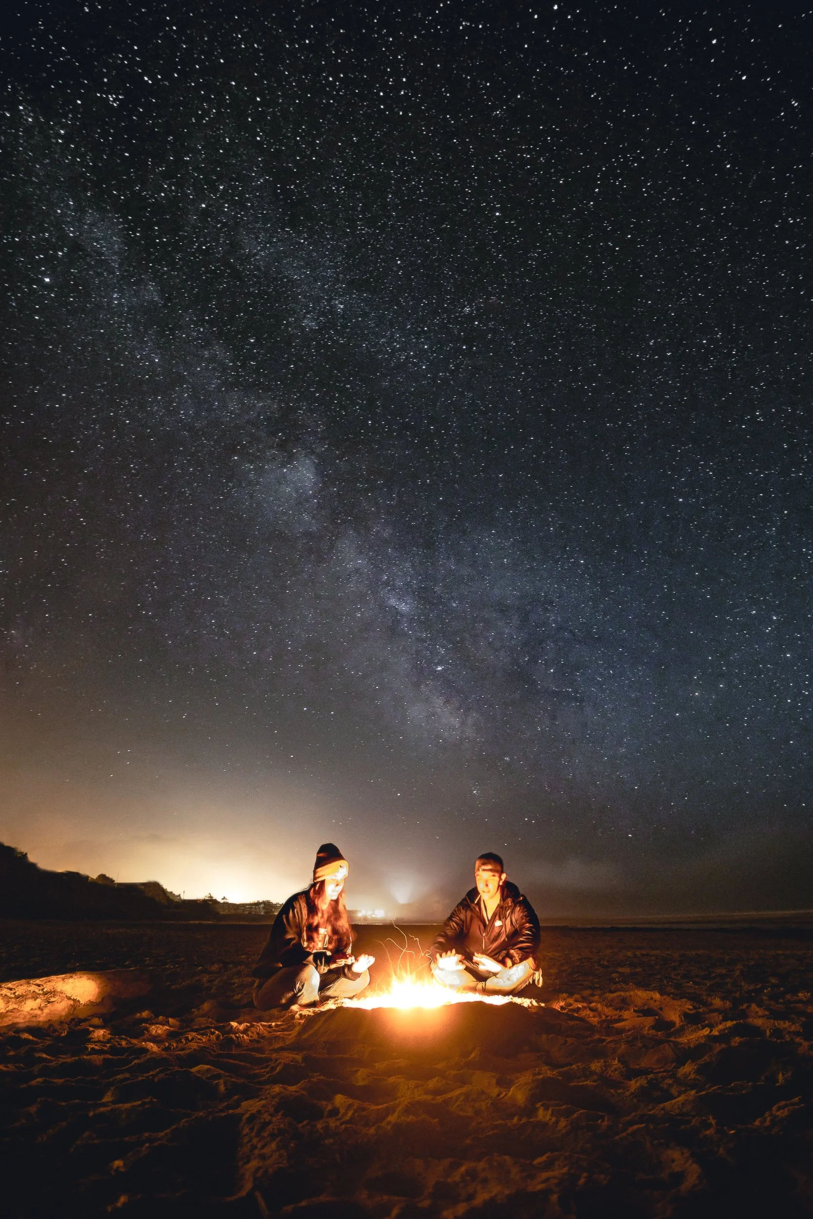 Two people by a beach bonfire under the Milky Way at Cannon Beach Oregon, astrophotography by James Brasier