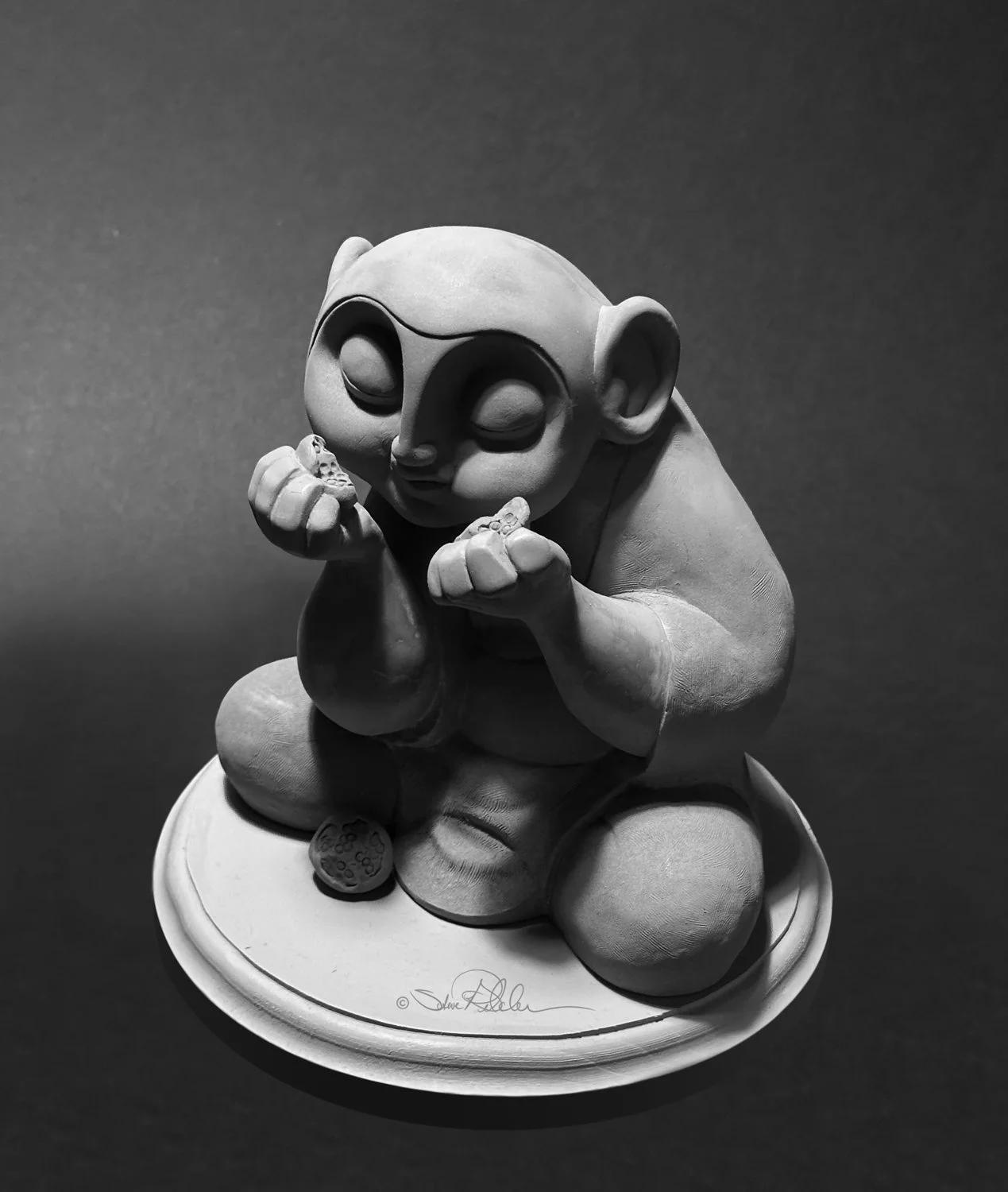 Sculpture in grey clay of buddha character sitting cross-legged eating a pomegranate fruit with his eyes closed.