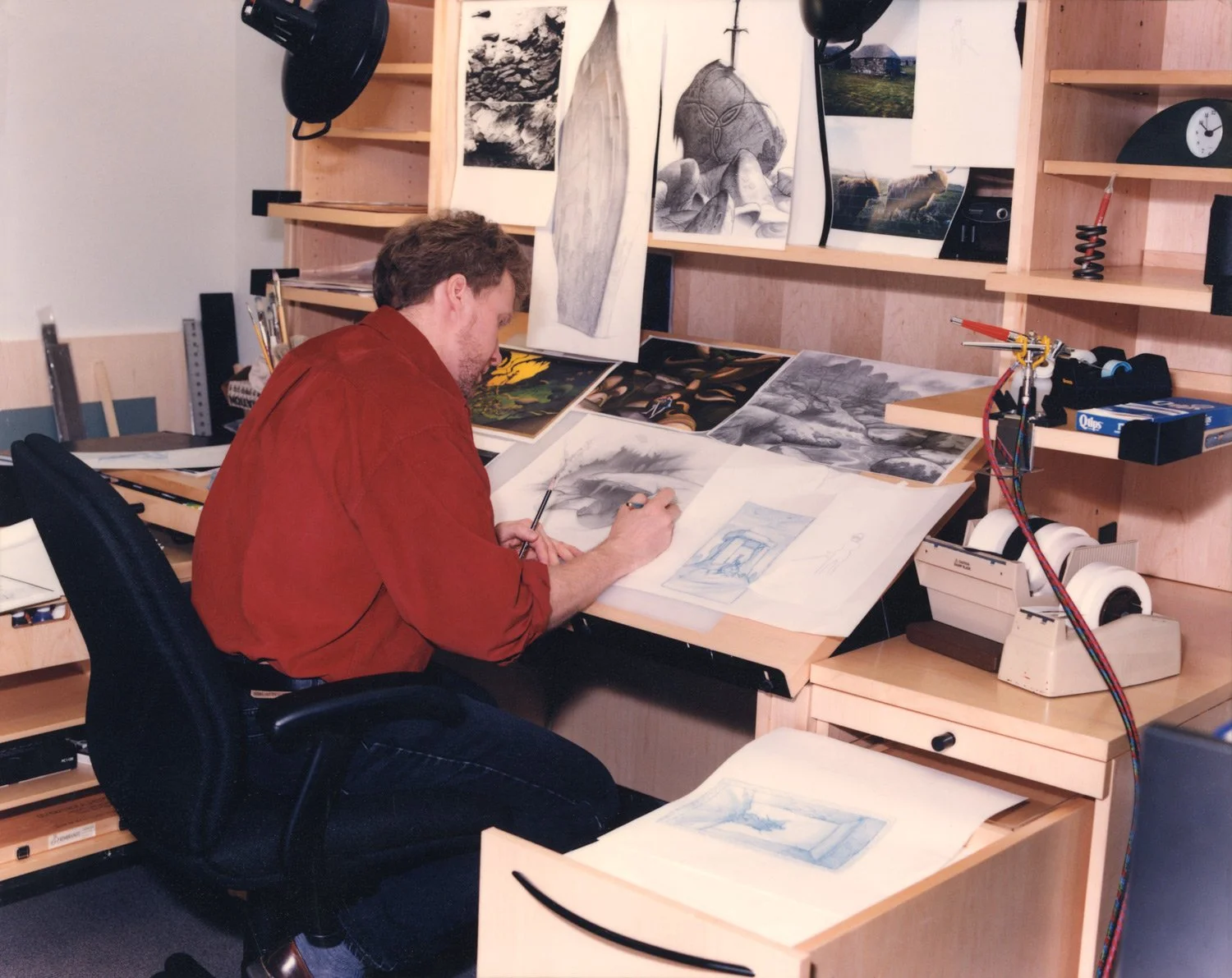Color photo of Steve Pilcher in a red shirt drawing at a drawing desk at Warner Bros. Feature animation.