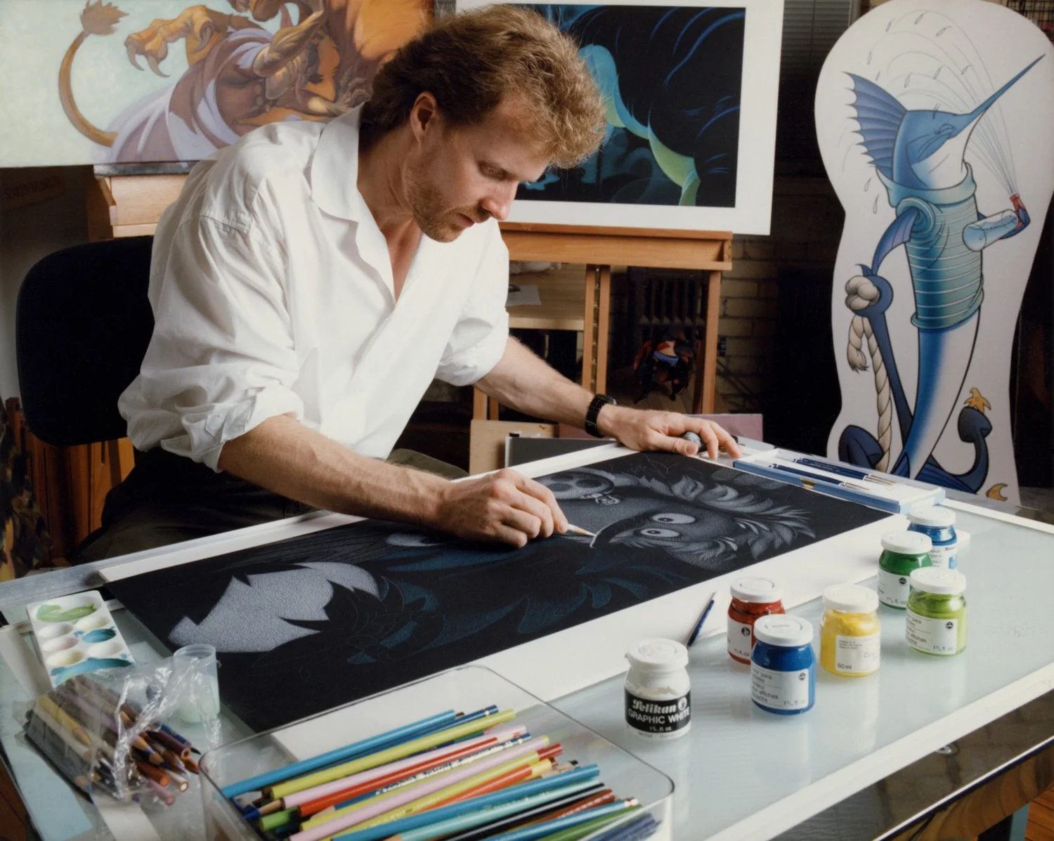 Color photo of Steve Pilcher dressed in a white shirt drawing with colored pencil on black paper in his Toronto studio.