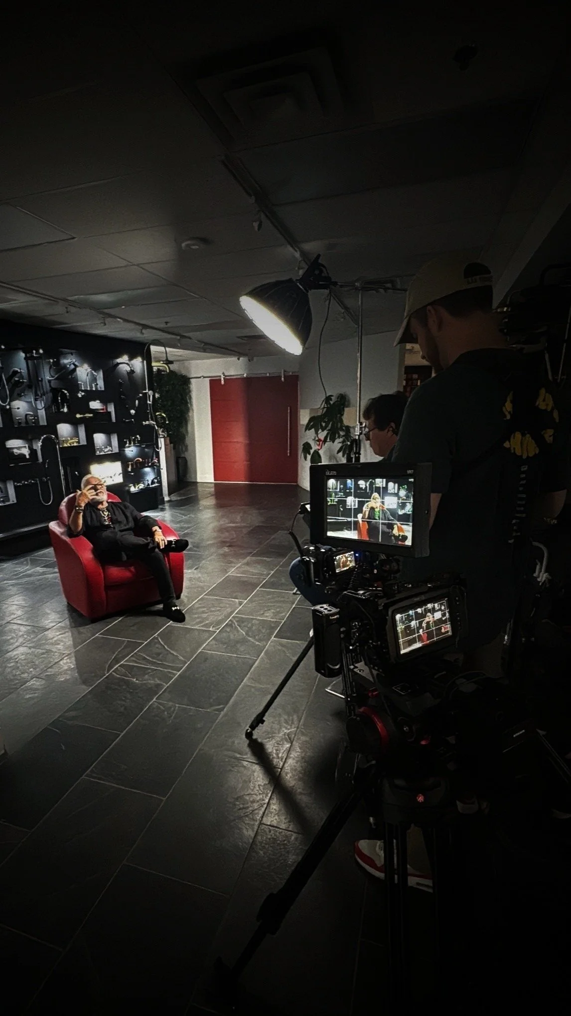 Filmmaking studio setup with person in red chair, film crew, camera equipment, studio lighting, and display monitors.