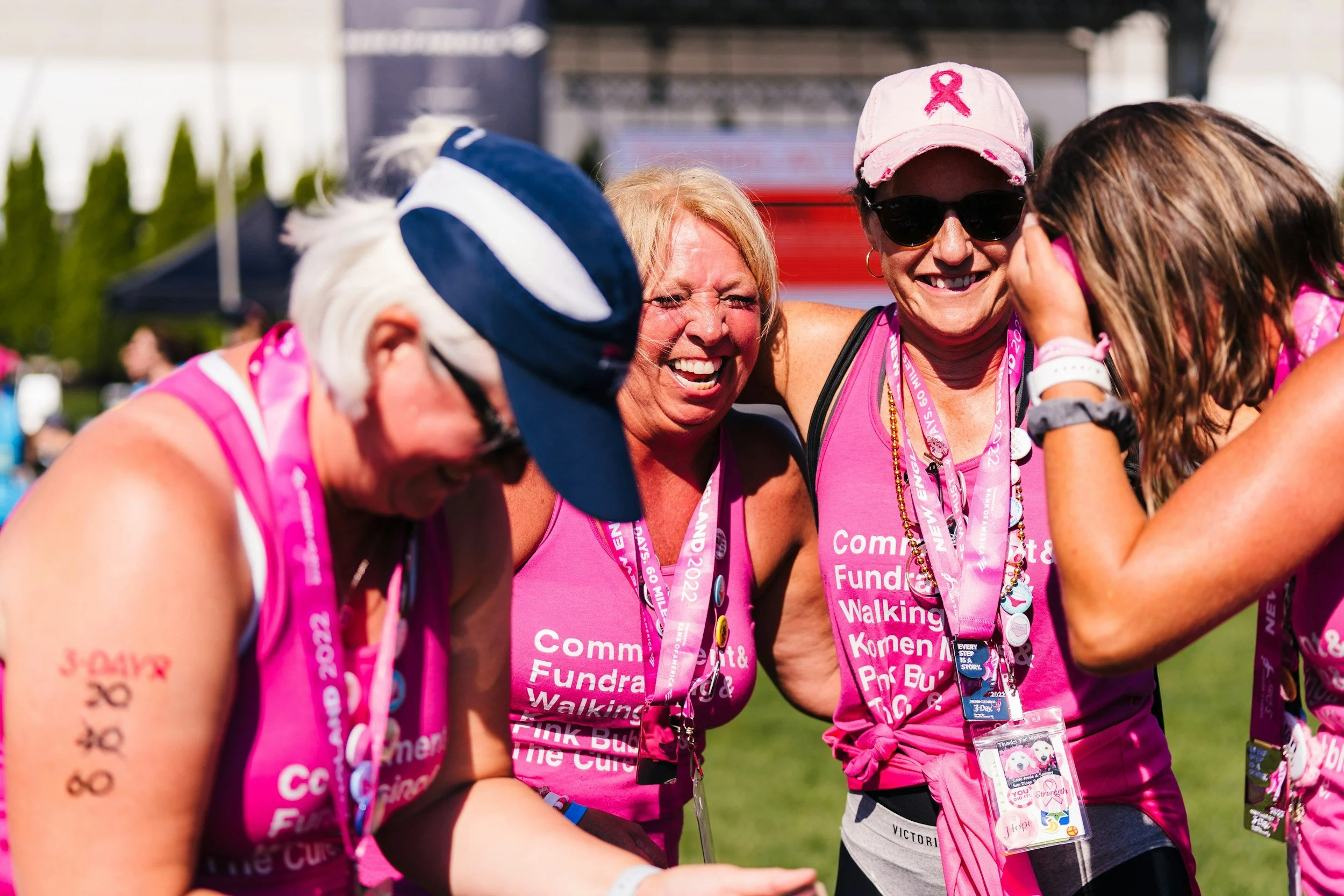Four women in pink shirts celebrating together at a charity walking event, wearing medals and pink ribbons for breast cancer awareness.
