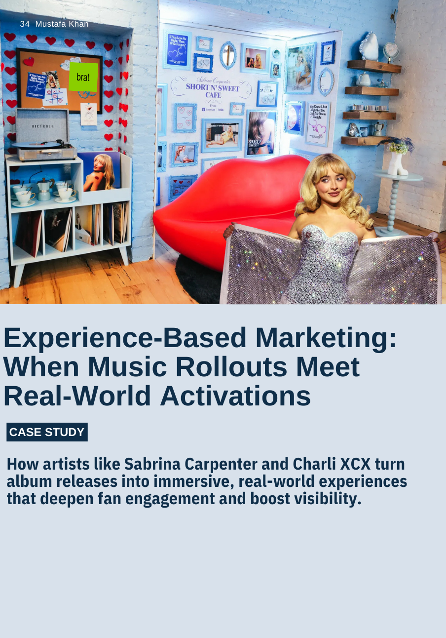 A young woman with blonde hair sits in a room with a large red lips-shaped sofa, surrounded by framed photos and wall decorations. The room has cozy, eclectic decor with a bookshelf, shelves with various decorative items, and wall art, creating a playful and artistic atmosphere.