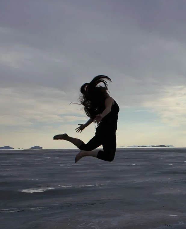 Person jumping in mid-air on a vast, flat landscape with a cloudy sky and distant islands in the background.
