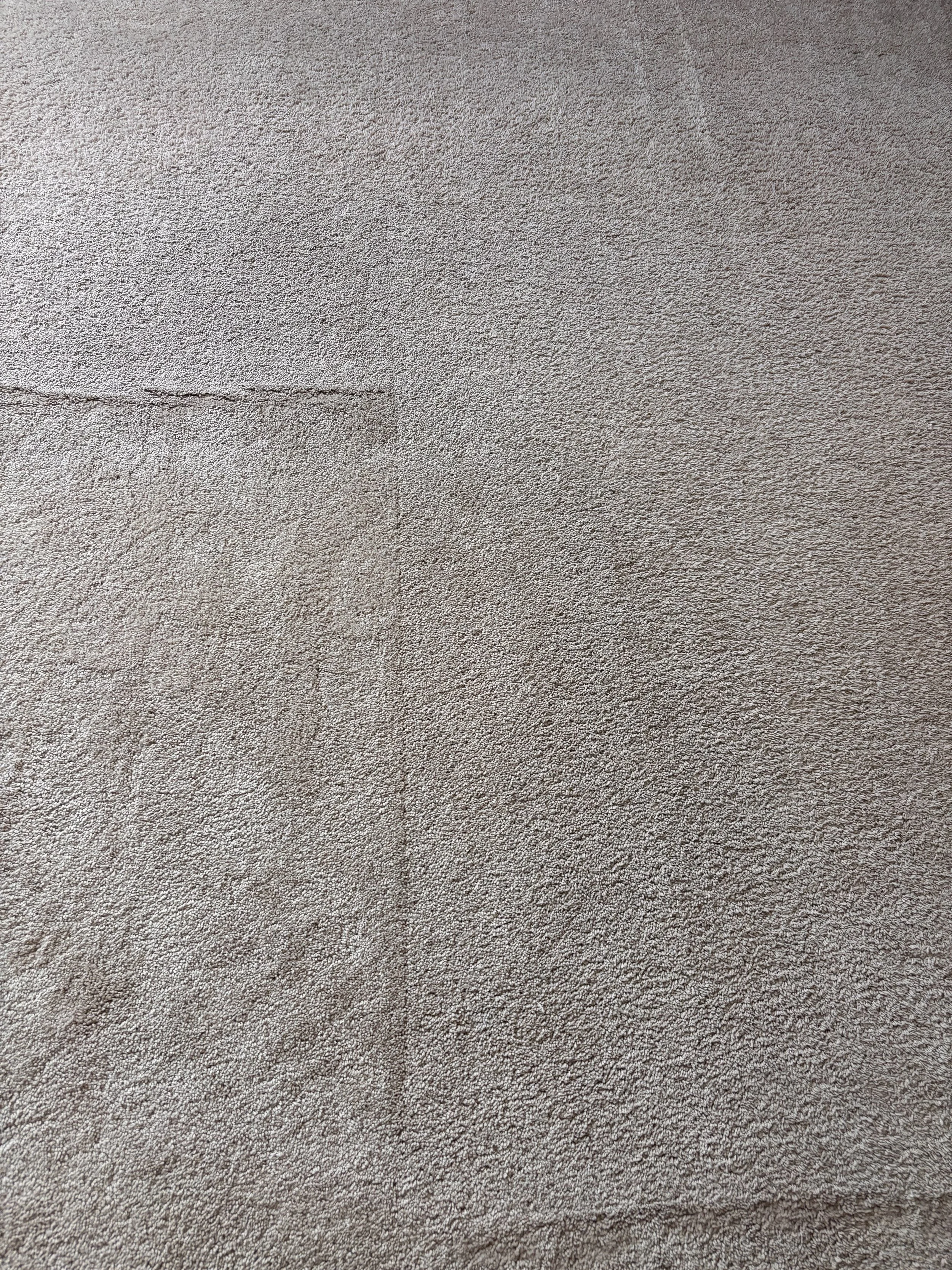 Close-up of a beige textured carpet with some dark streaks and lines.