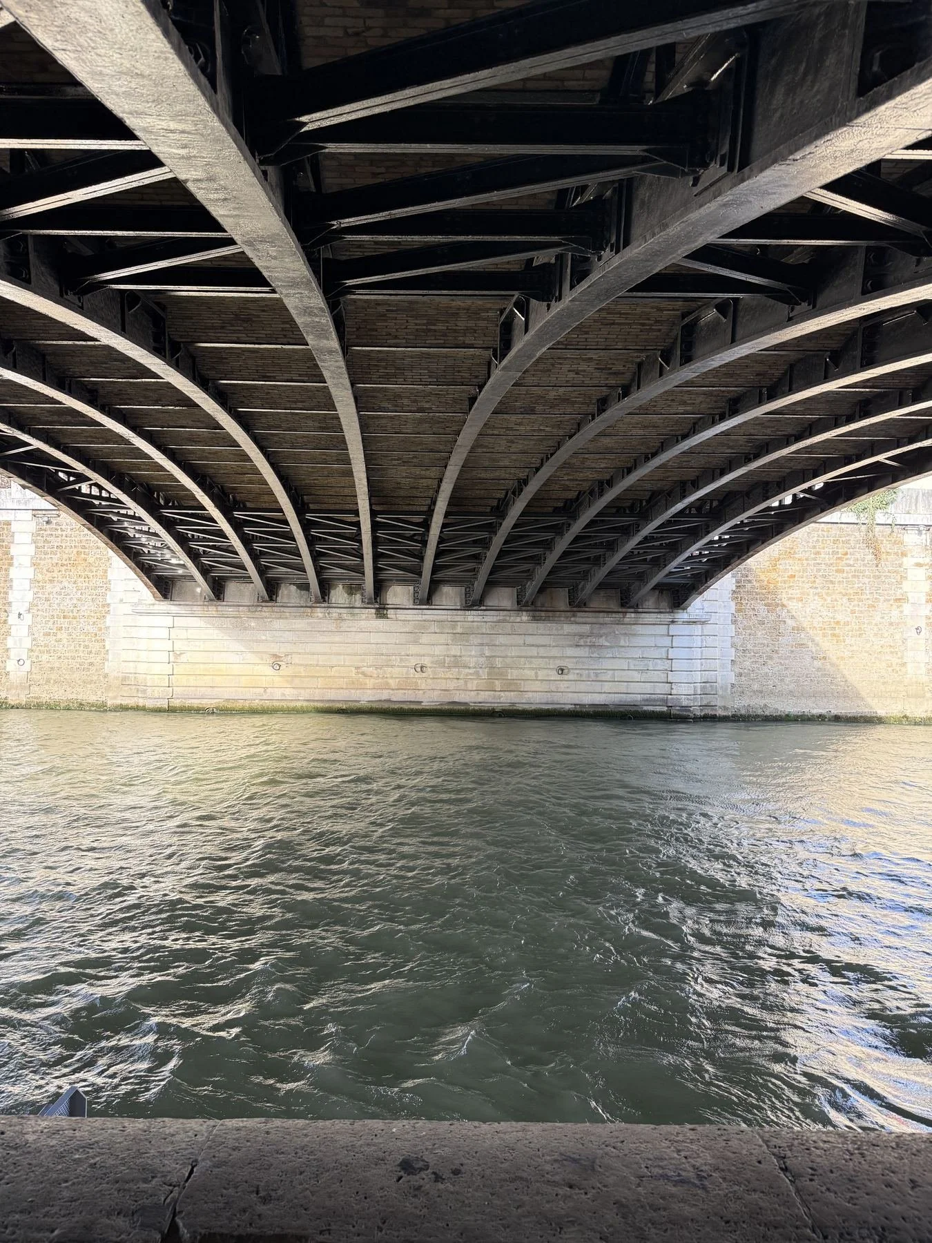 Underneath a bridge over a river, showing the bridge's underside structure and water below.