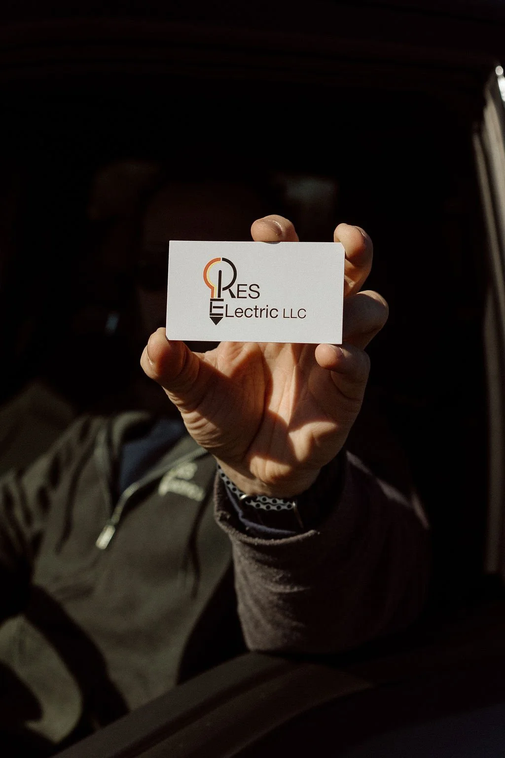 A person holding a business card for RES Electric LLC, with the logo of a light bulb incorporating an electrical plug.