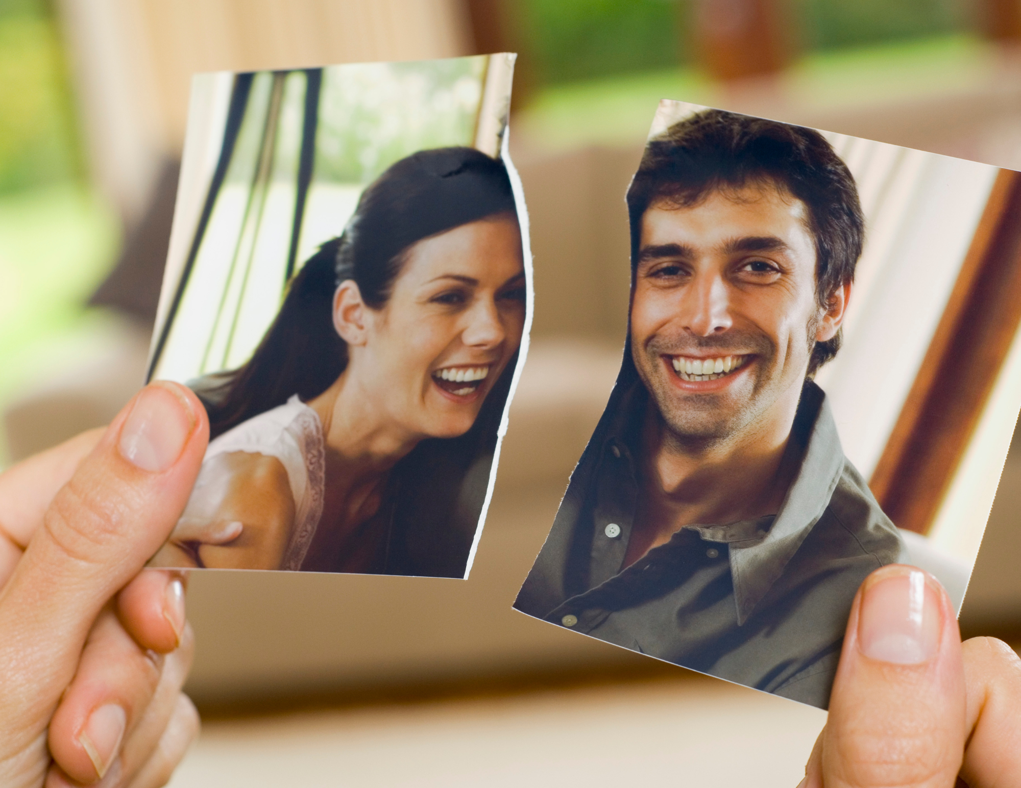 Close-up of two photographs of a smiling man and woman being held by a person's fingers.