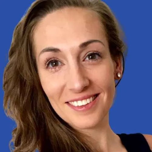 A woman with long, wavy light brown hair, smiling, wearing pearl earrings and a dark top, against a blue background.