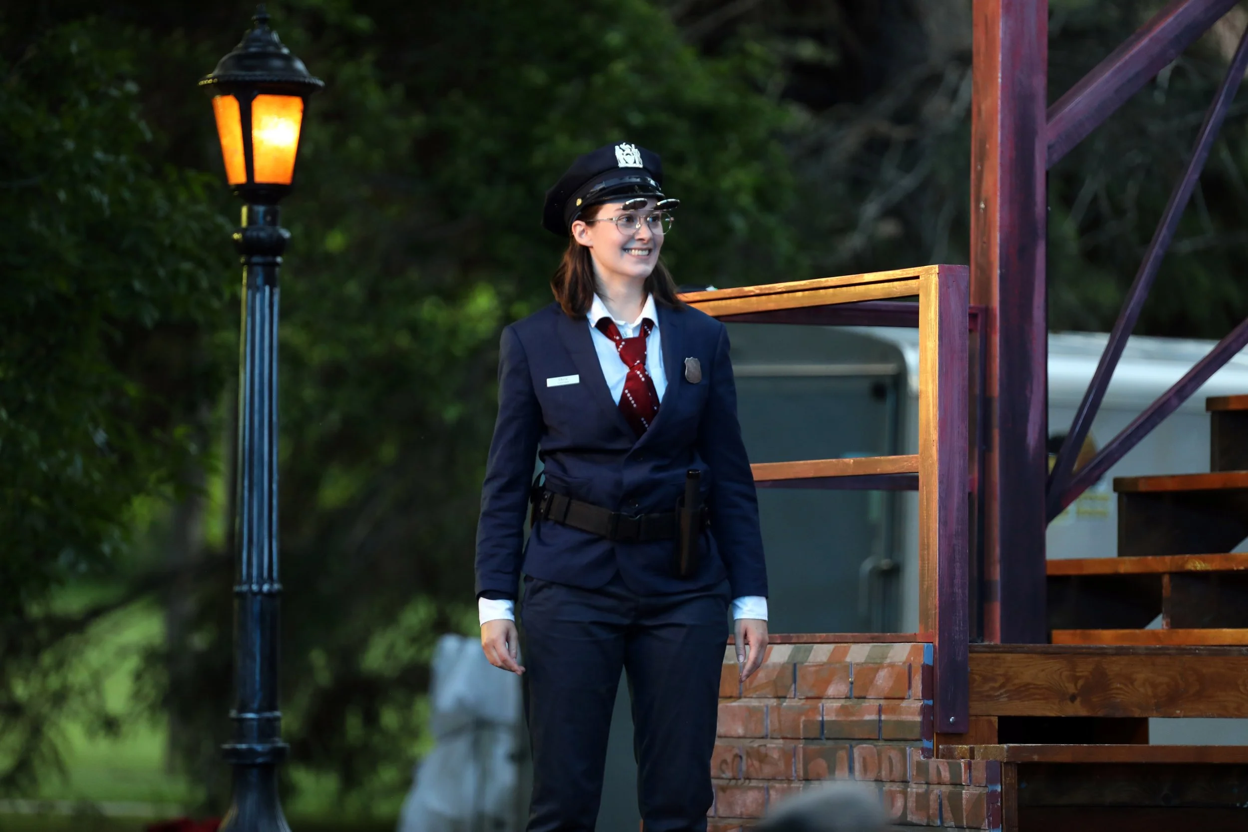 Emily Michelle Walton as Elbow in Measure for Measure at Montana Shakespeare in the Parks, smiling in a police uniform on an outdoor stage.