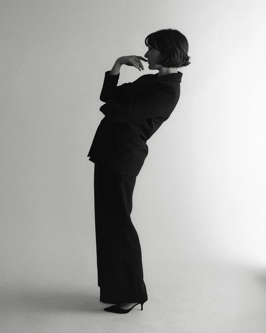 Studio portrait of actor Emily Michelle Walton in profile, wearing a black suit with one hand resting near her mouth.