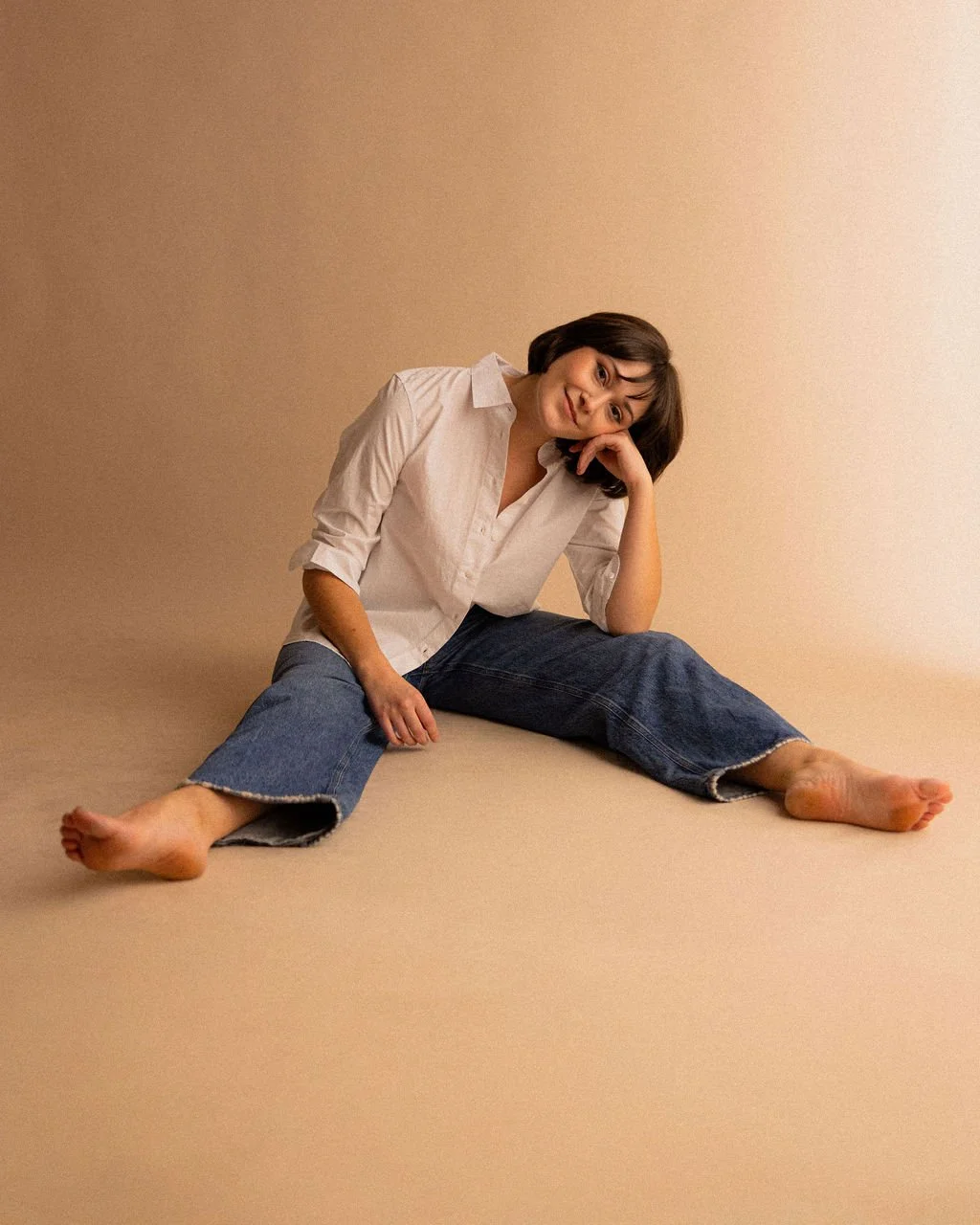 Studio portrait of actor Emily Michelle Walton seated on the floor with her legs outstretched, smiling.