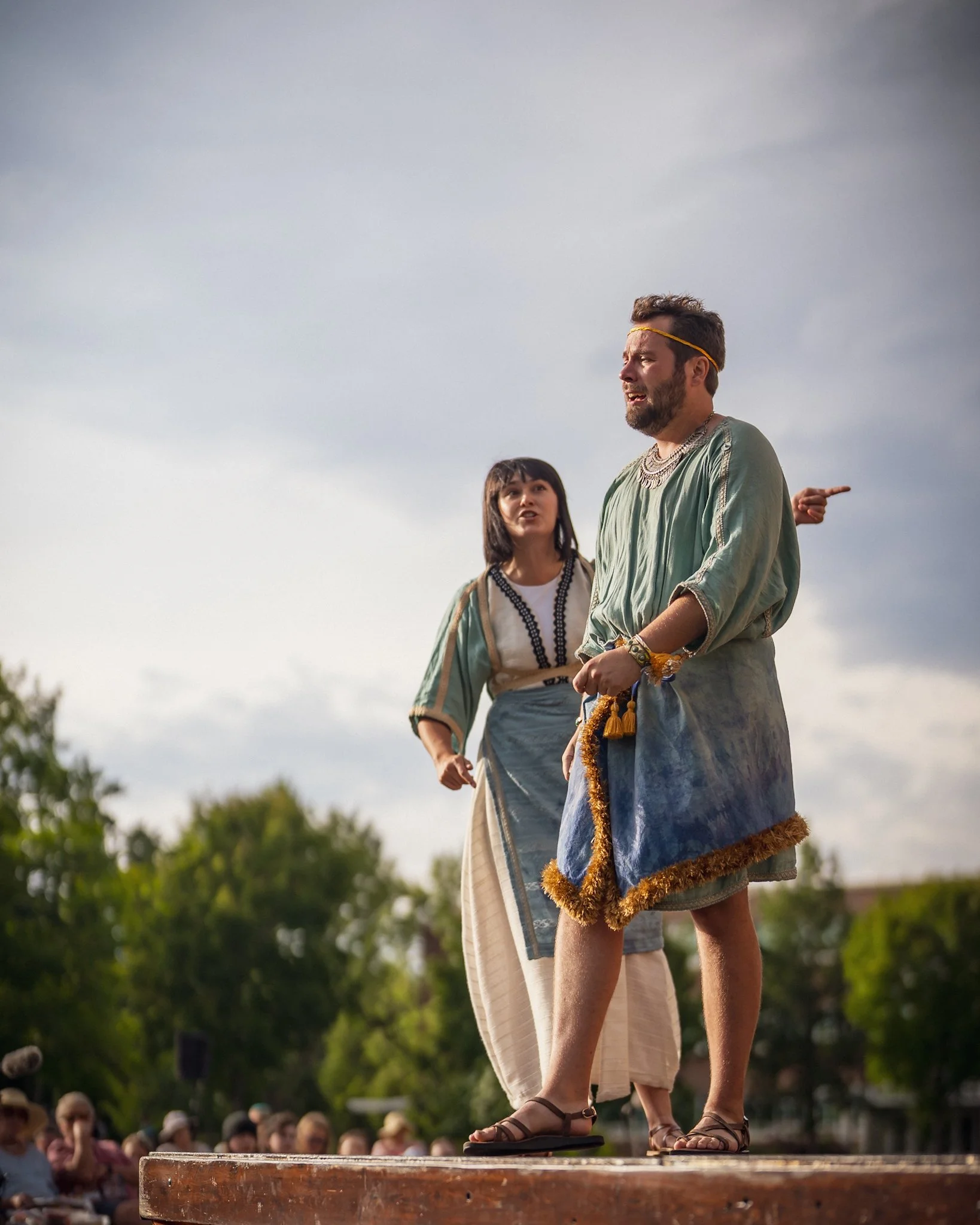 Emily Michelle Walton as Camillo and Sam Cheeseman as Leontes in The Winter's Tale at Montana Shakespeare in the Parks, performing outdoors in Mycenaean-inspired costumes.