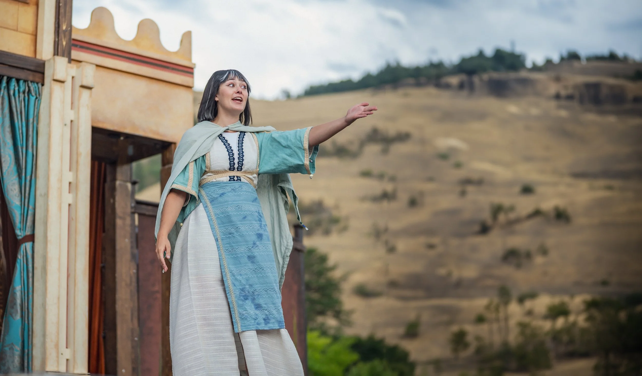 Emily Michelle Walton as Camillo in The Winter's Tale at Montana Shakespeare in the Parks, extending one hand while wearing a Mycenaean-inspired costume.