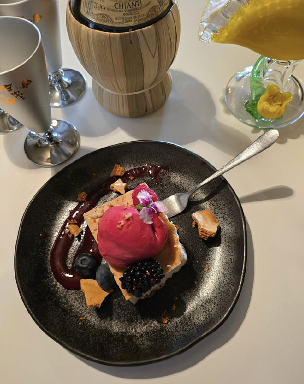 Dessert plate with berry sorbet, blueberries, blackberries, and crumbled cookies, garnished with an edible flower, served with berry sauce on a black plate.