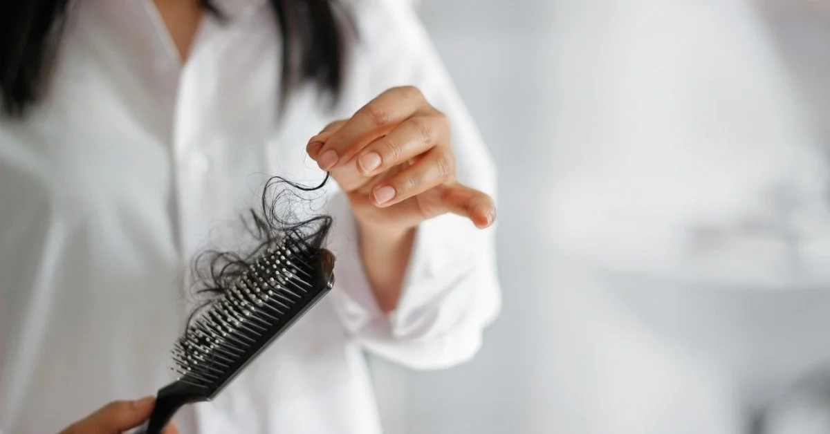 A woman holding a hairbrush with a bunch of hair on it. She is pulling a string of hair off of the brush.