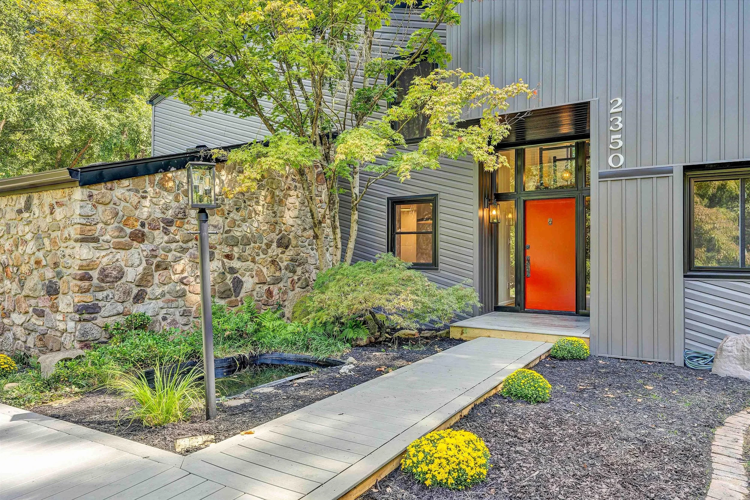 Front porch of a house with a white door, black lantern-style exterior lights, potted red flowering plants, and white siding.