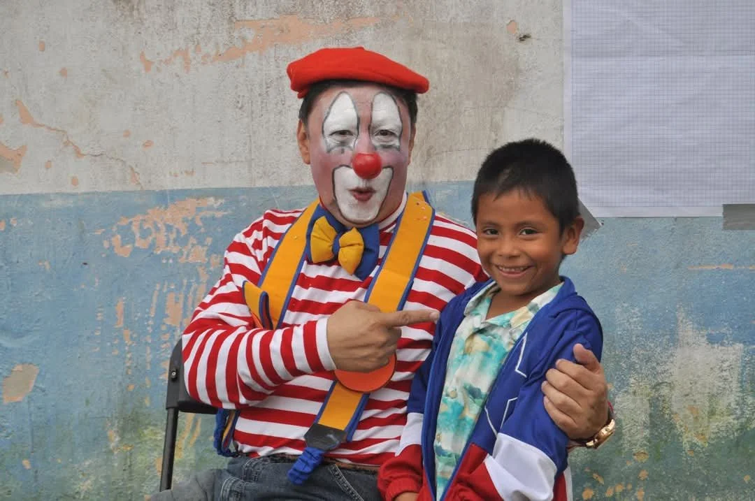 Voluntario vestido de payaso, alegrando a niños en un evento recreativo.