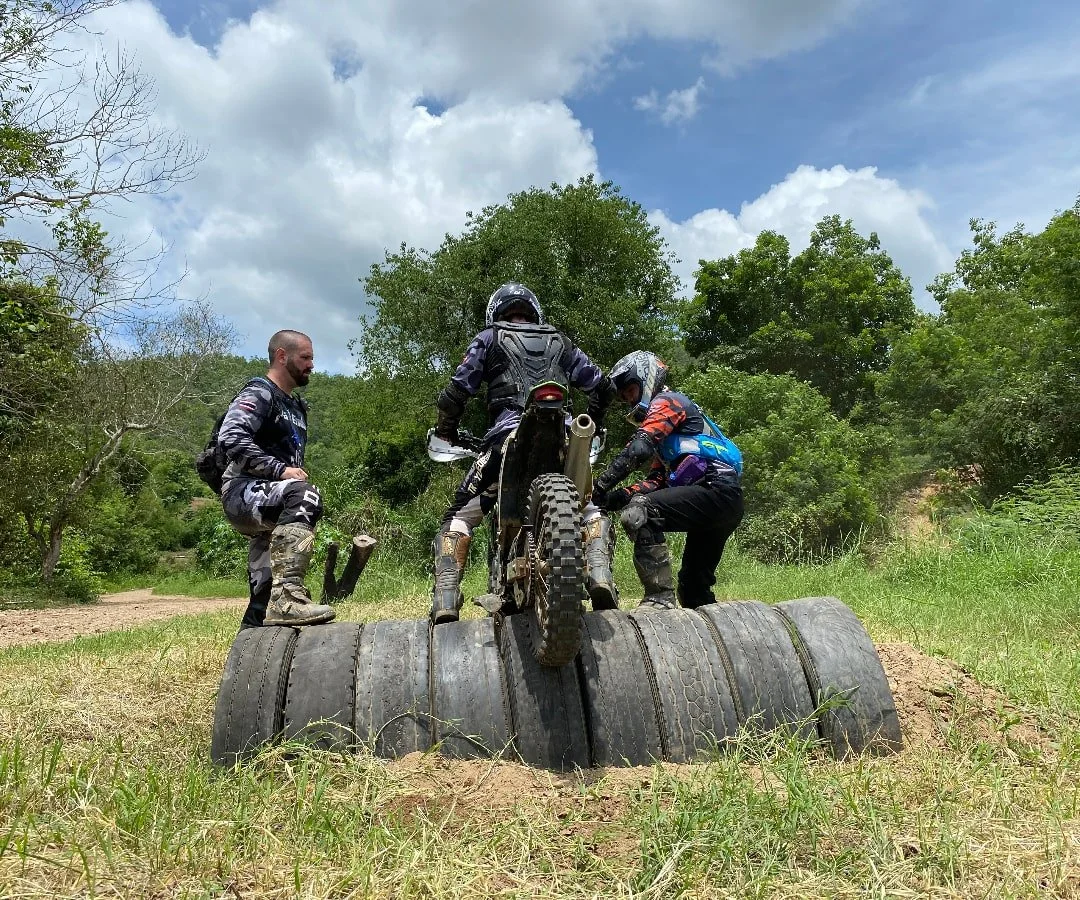 Four off-road motorcycle riders practicing on a trail with tires and trees.